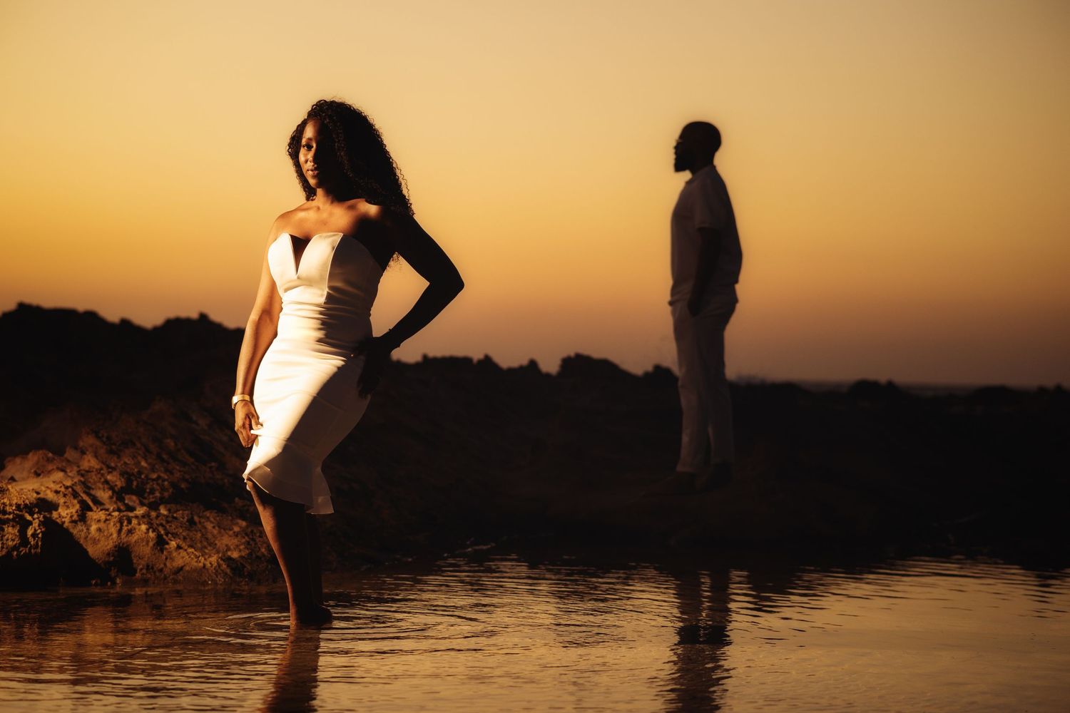 Artistic silhouette portrait of couple by water during golden hour sunset.