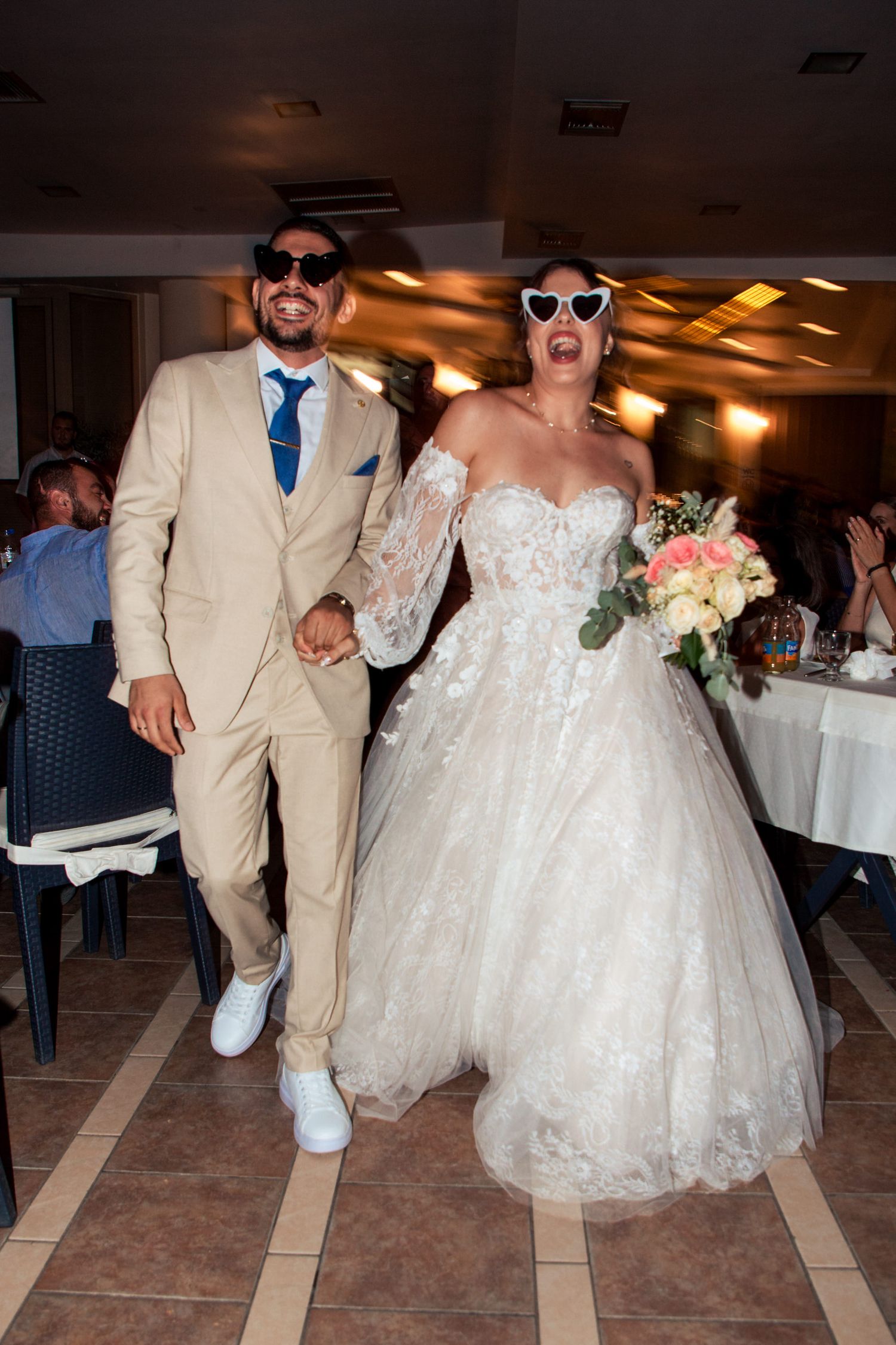 Wedding party dances in reception venue wearing sunglasses and formal attire.