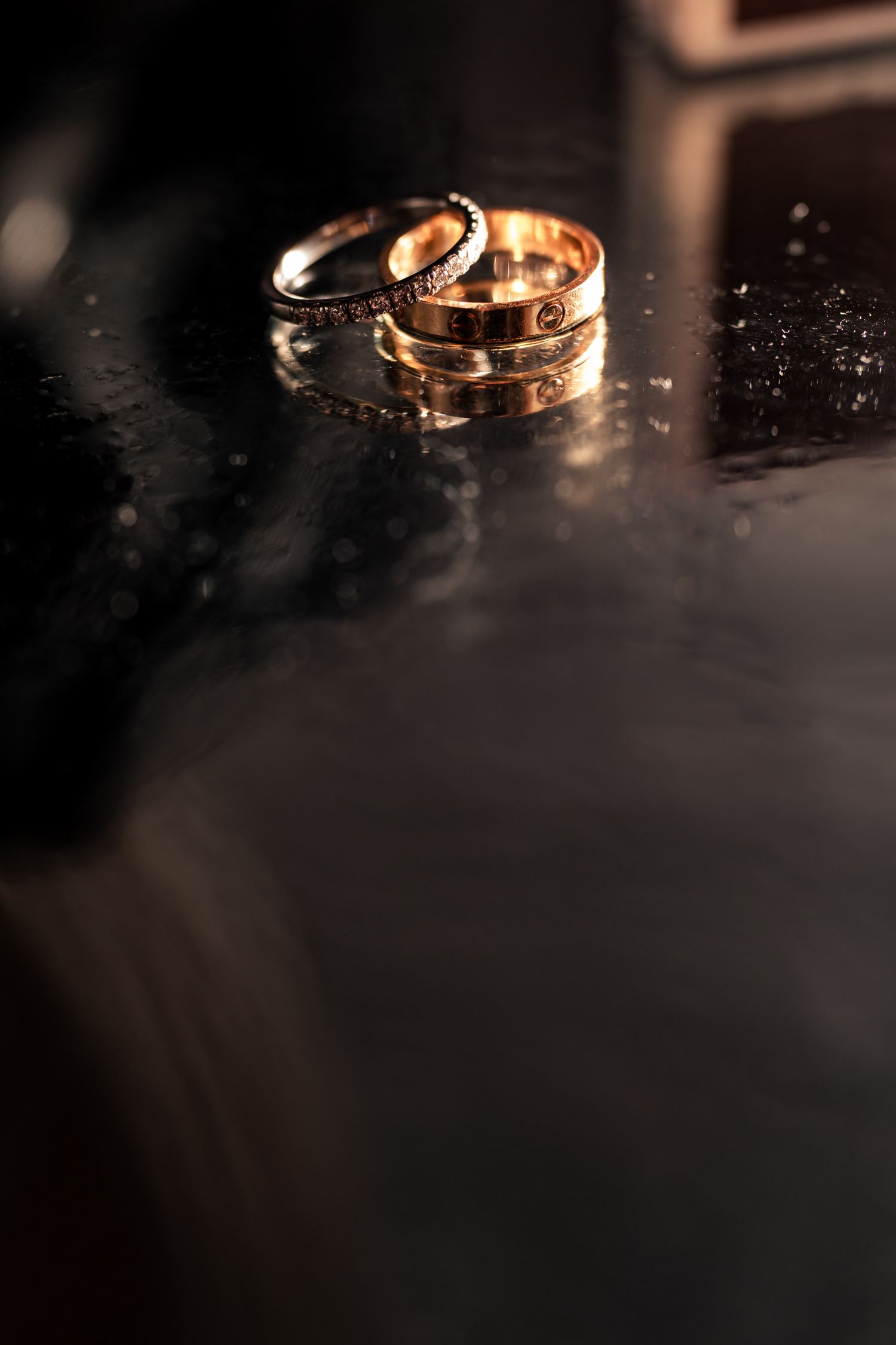 Close-up macro shots of wedding rings with dramatic lighting on dark reflective surface.