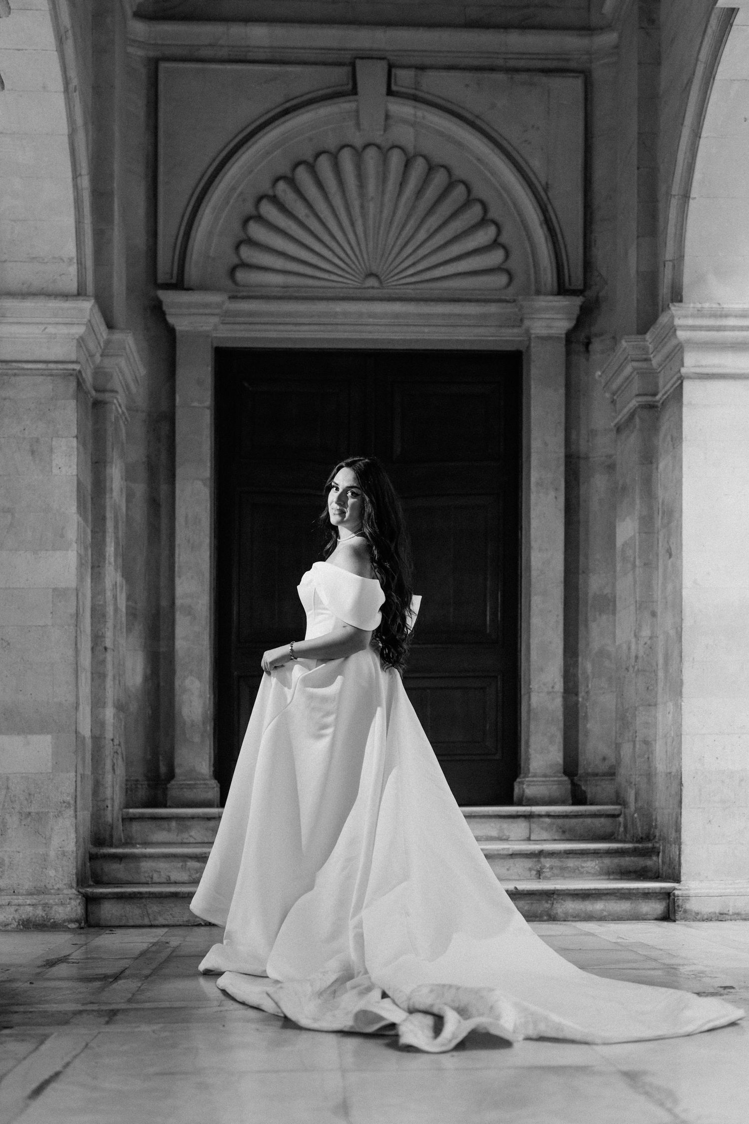 Flowing wedding dress train creates dramatic silhouette against classical architecture.