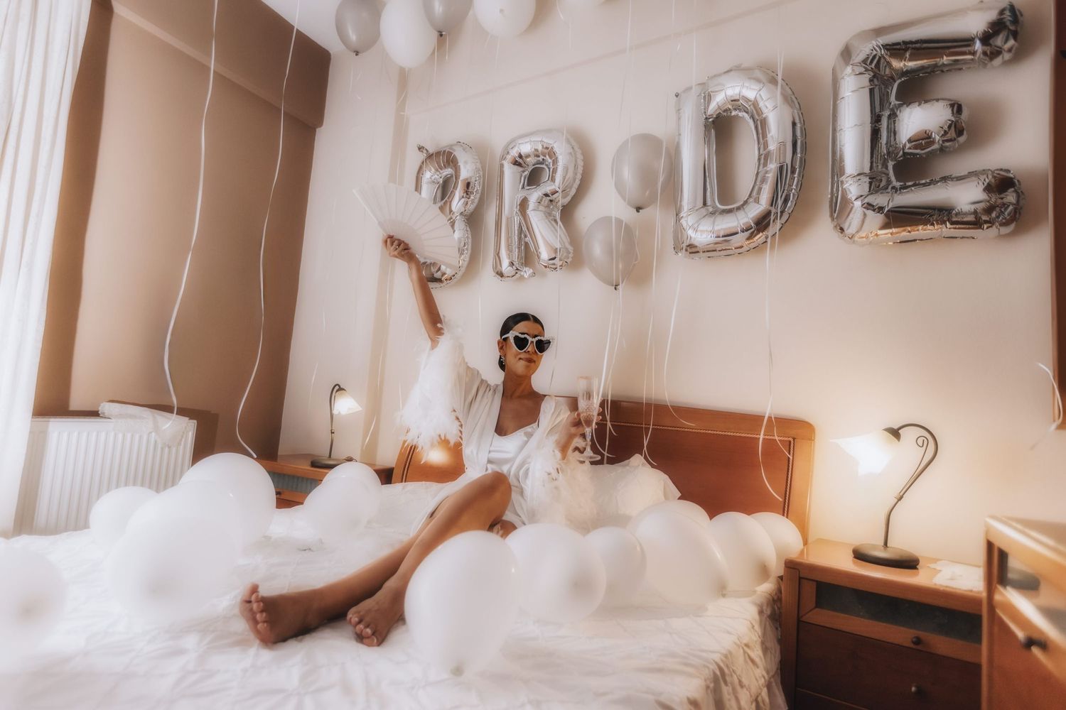 White balloon decorations and silver letter balloons spelling out 'BRIDE' in a bright room.