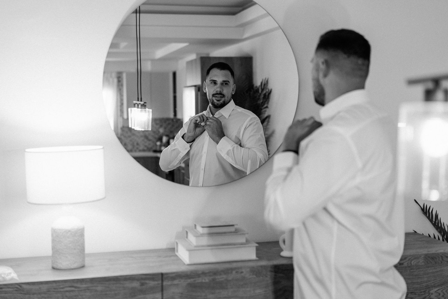 Black and white image of someone adjusting a tie in a circular mirror.