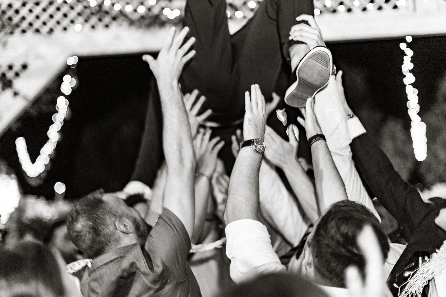 Black and white photo of wedding guests with raised hands dancing at reception.