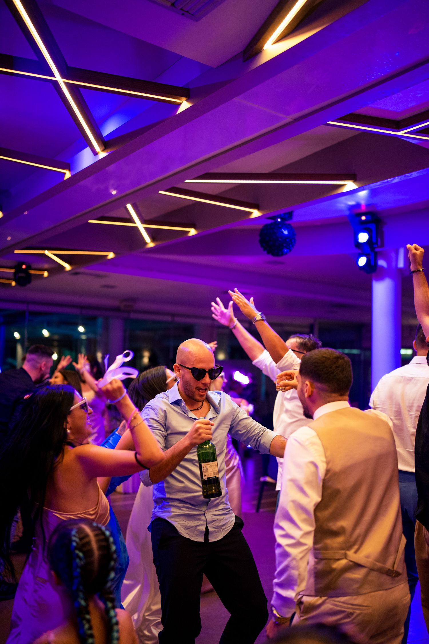 People dancing under purple lighting with geometric ceiling patterns at a celebration.