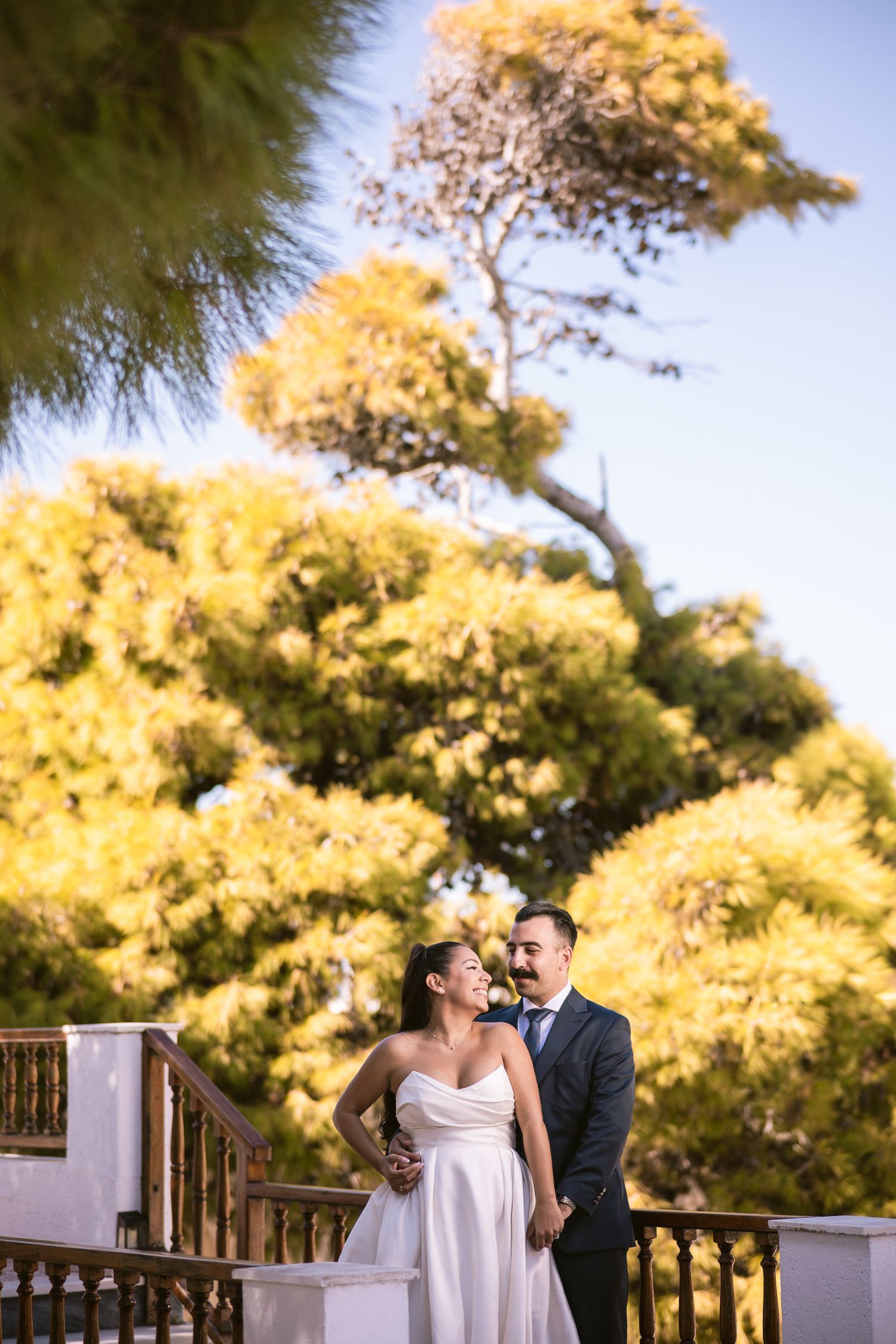 A wedding couple shares an intimate moment on a balcony surrounded by autumn foliage.