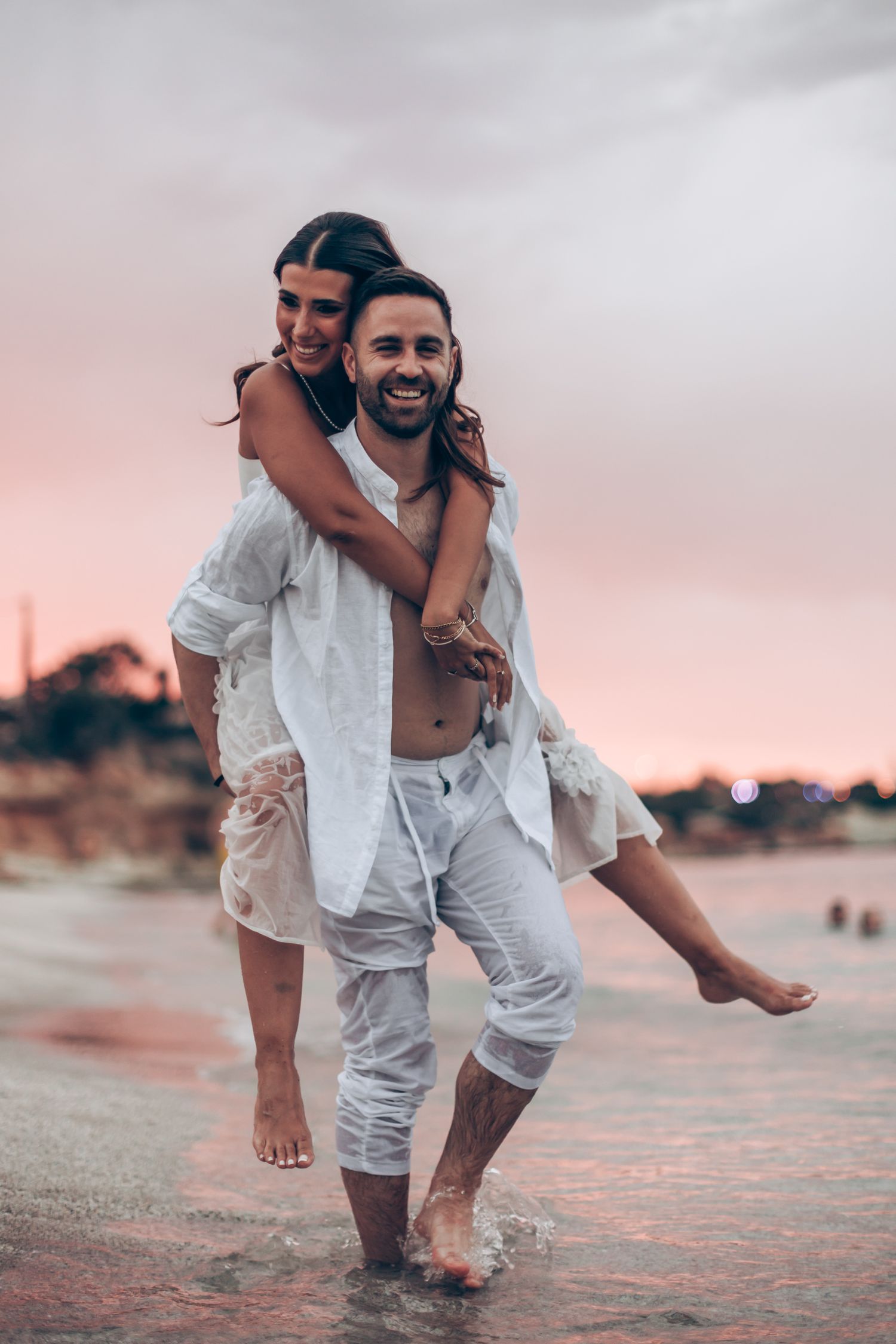 Joyful couple plays and laughs on beach during sunset engagement session.
