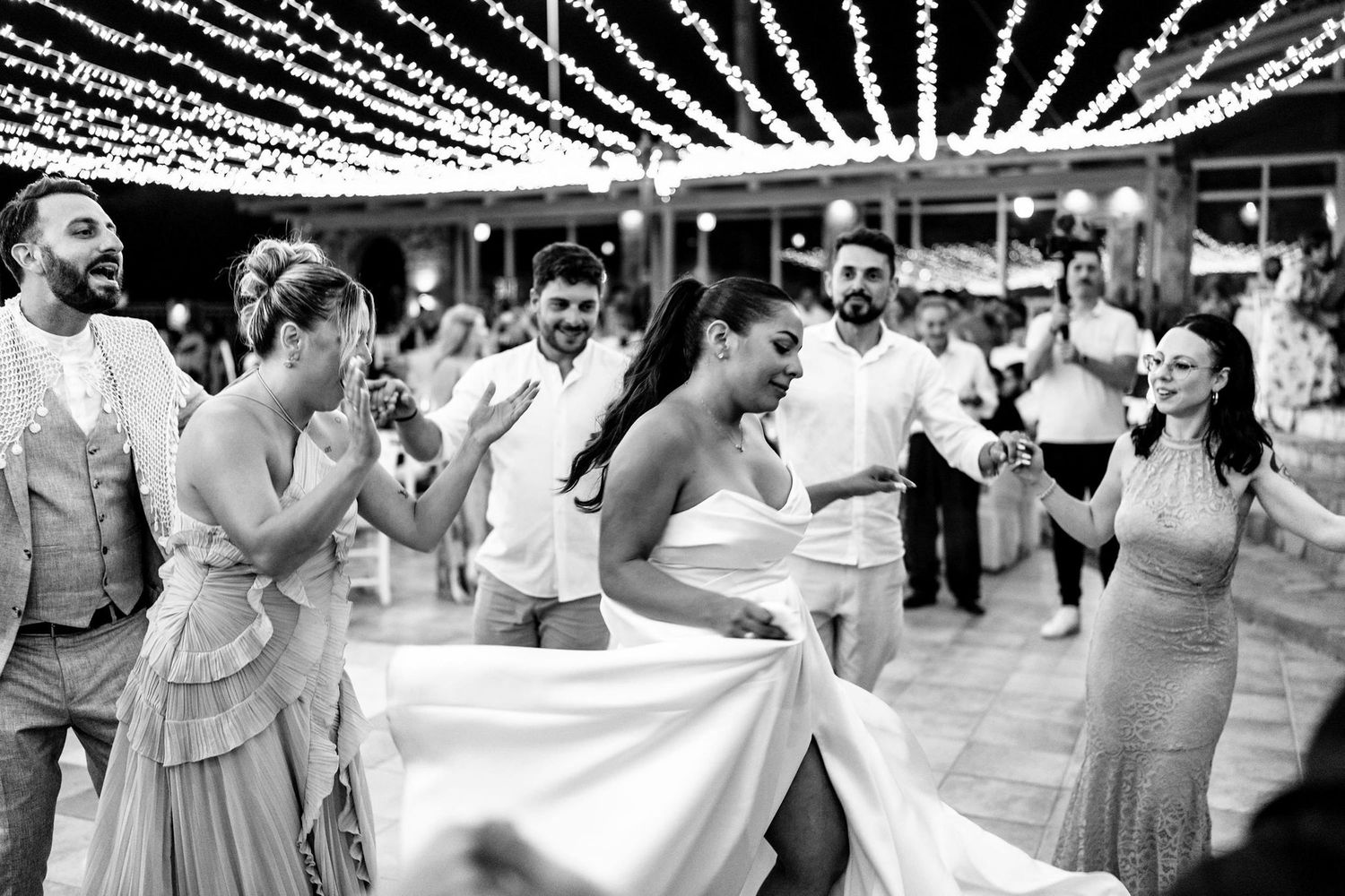 Wedding guests dance together under string lights at an outdoor reception.