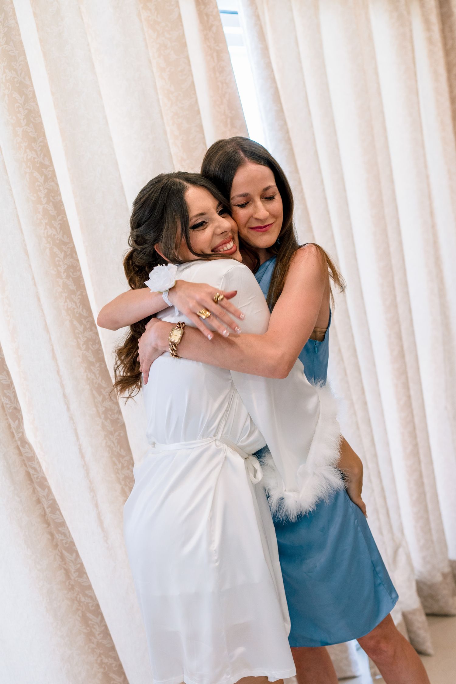 Friends sharing warm embraces in a room with white curtains.
