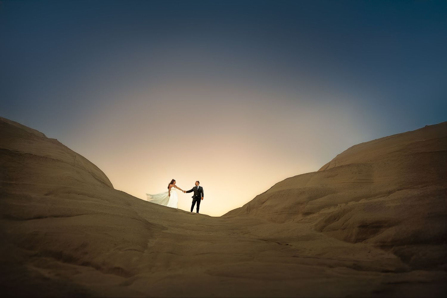 Silhouettes of figures walking along desert dunes at sunset.