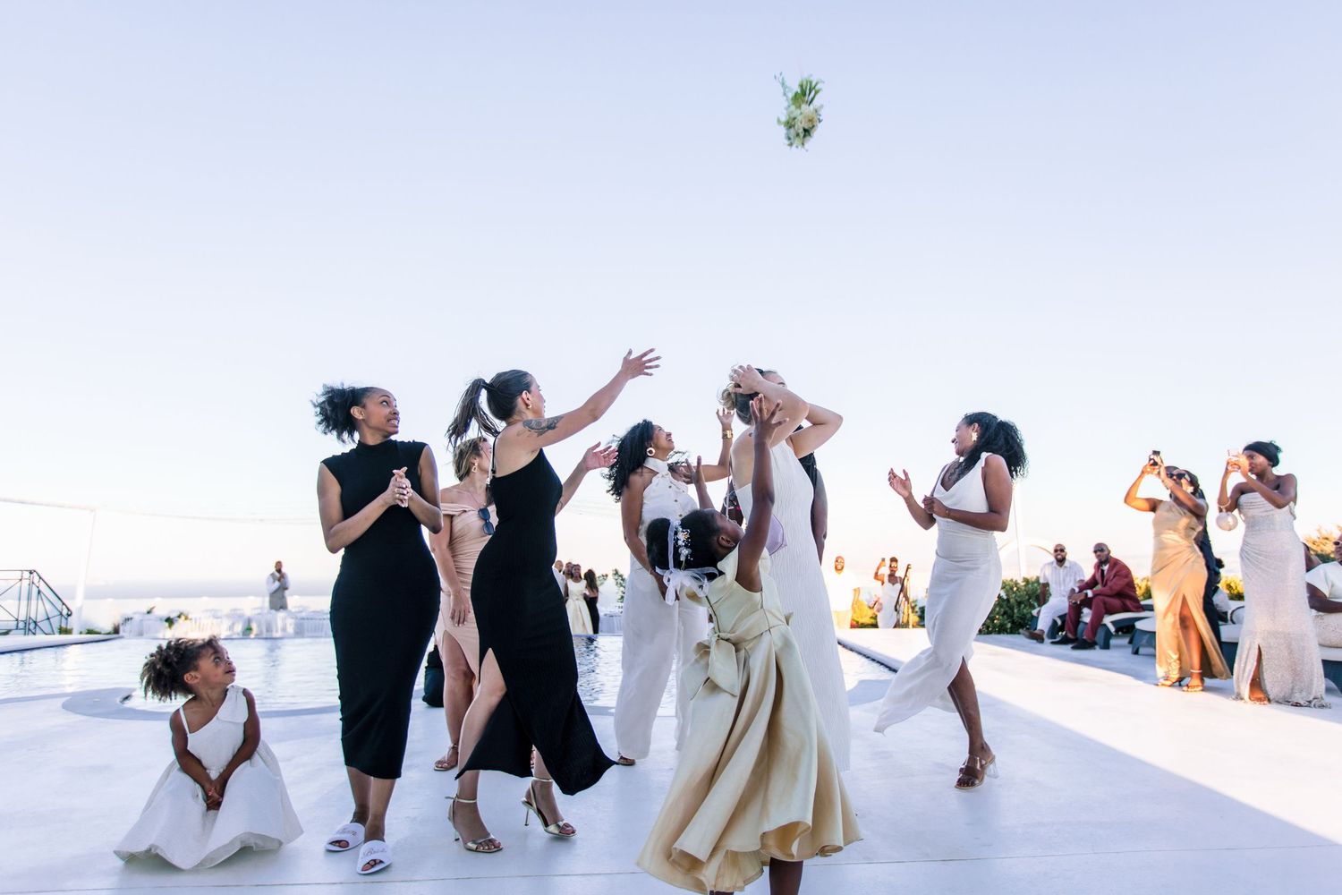 Group of wedding guests in white attire dancing on an outdoor terrace.
