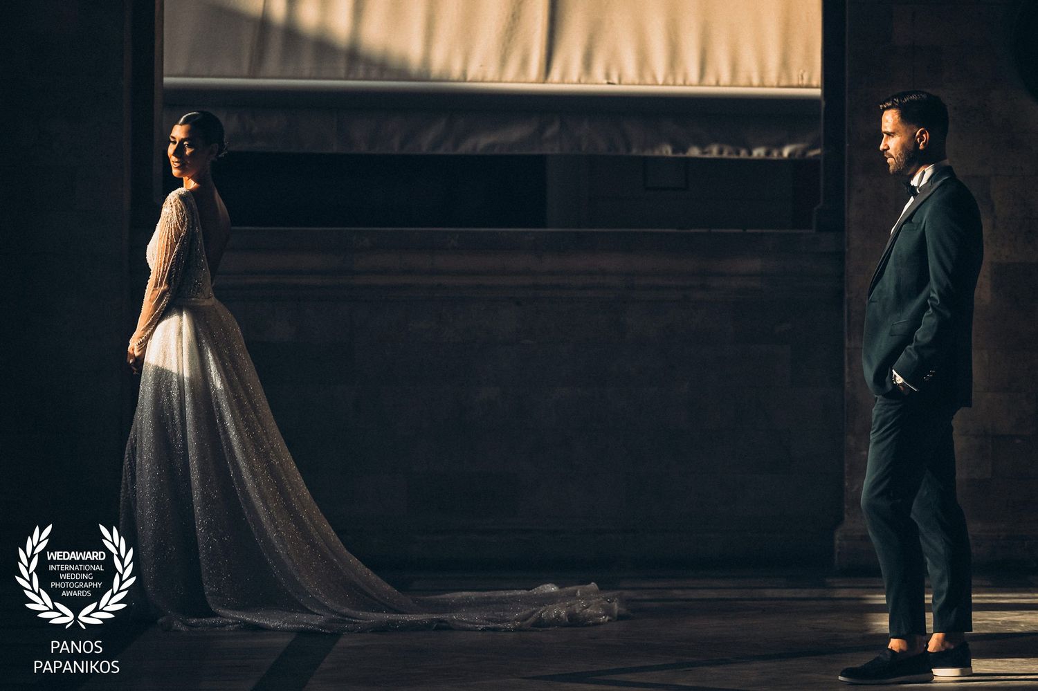 Dramatic wedding portrait showing silhouettes of couple standing apart in dark moody lighting with flowing dress train.