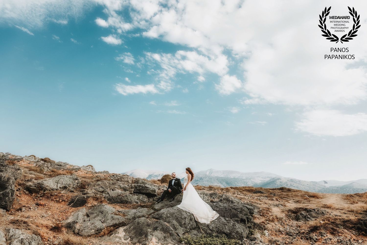Destination wedding photography against blue sky and rocky coastal terrain.