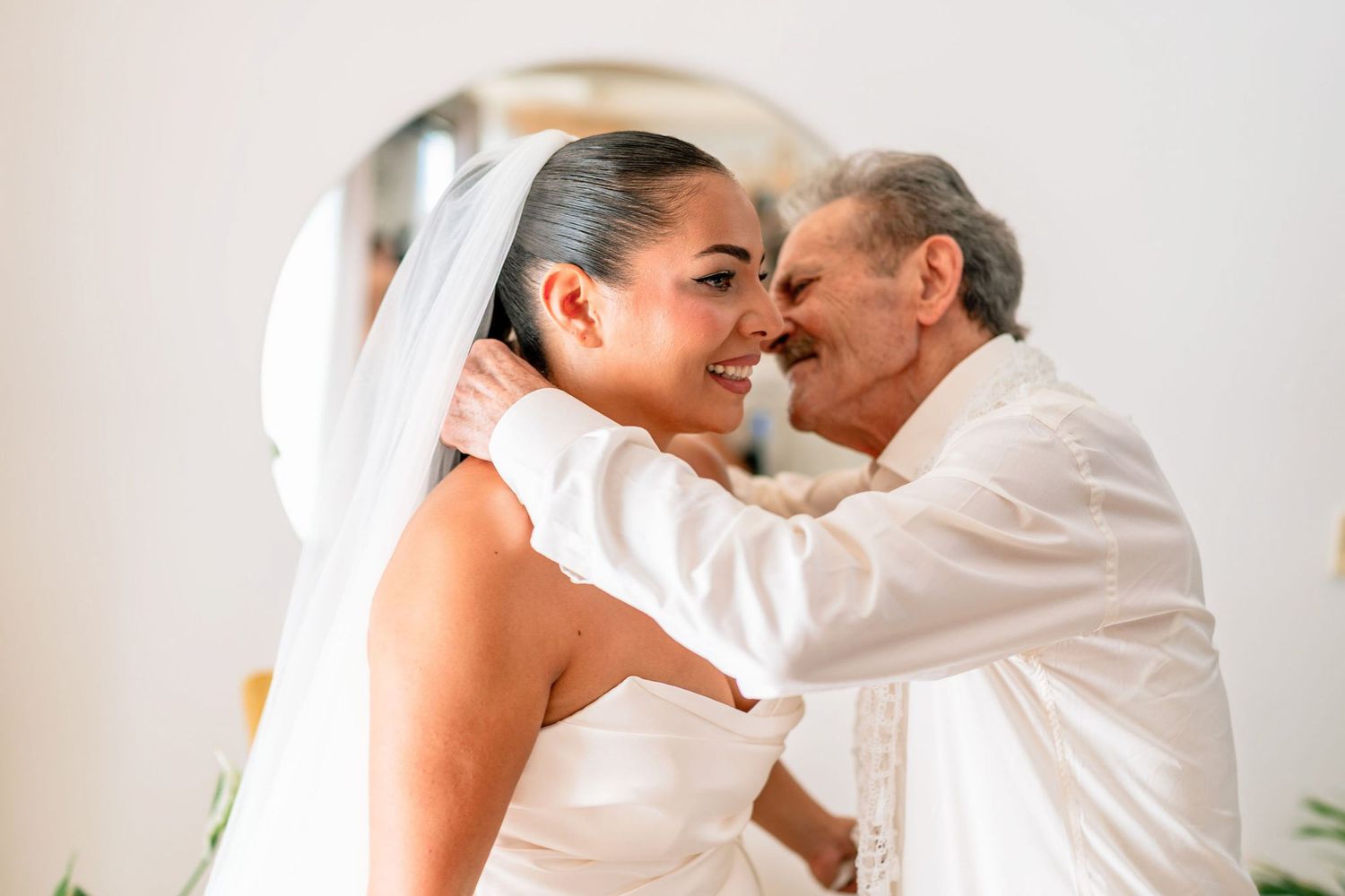 Intimate wedding moment captured in soft natural light against white background.