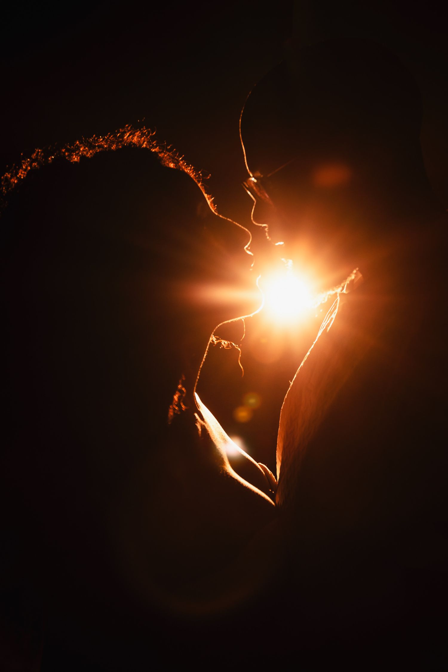 Backlit couple in intimate embrace with glowing sunburst effect.