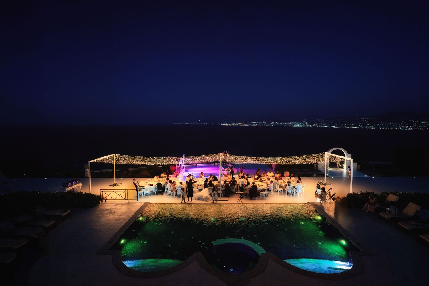 An outdoor wedding reception venue lit up at night with ocean views and colorful lighting.