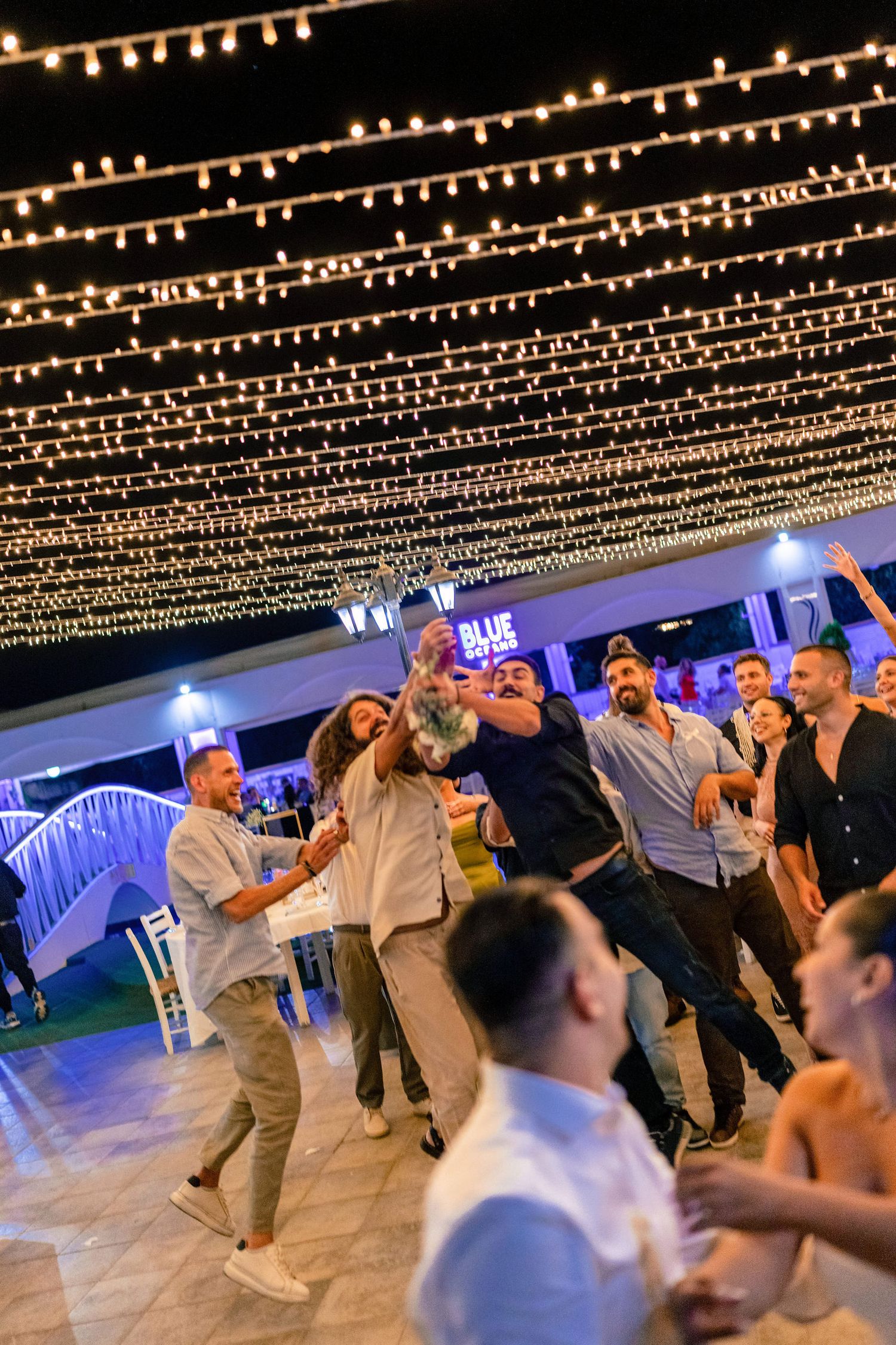 Guests dance beneath a canopy of twinkling string lights at an outdoor wedding celebration.