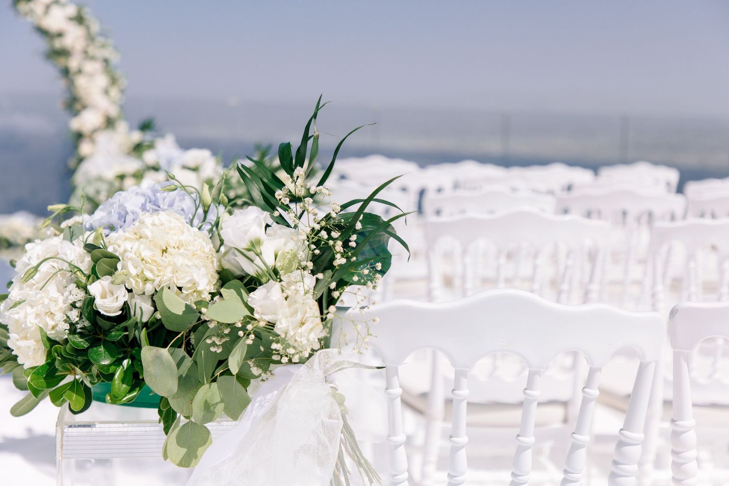 White floral arrangements and greenery decorating outdoor wedding ceremony space.
