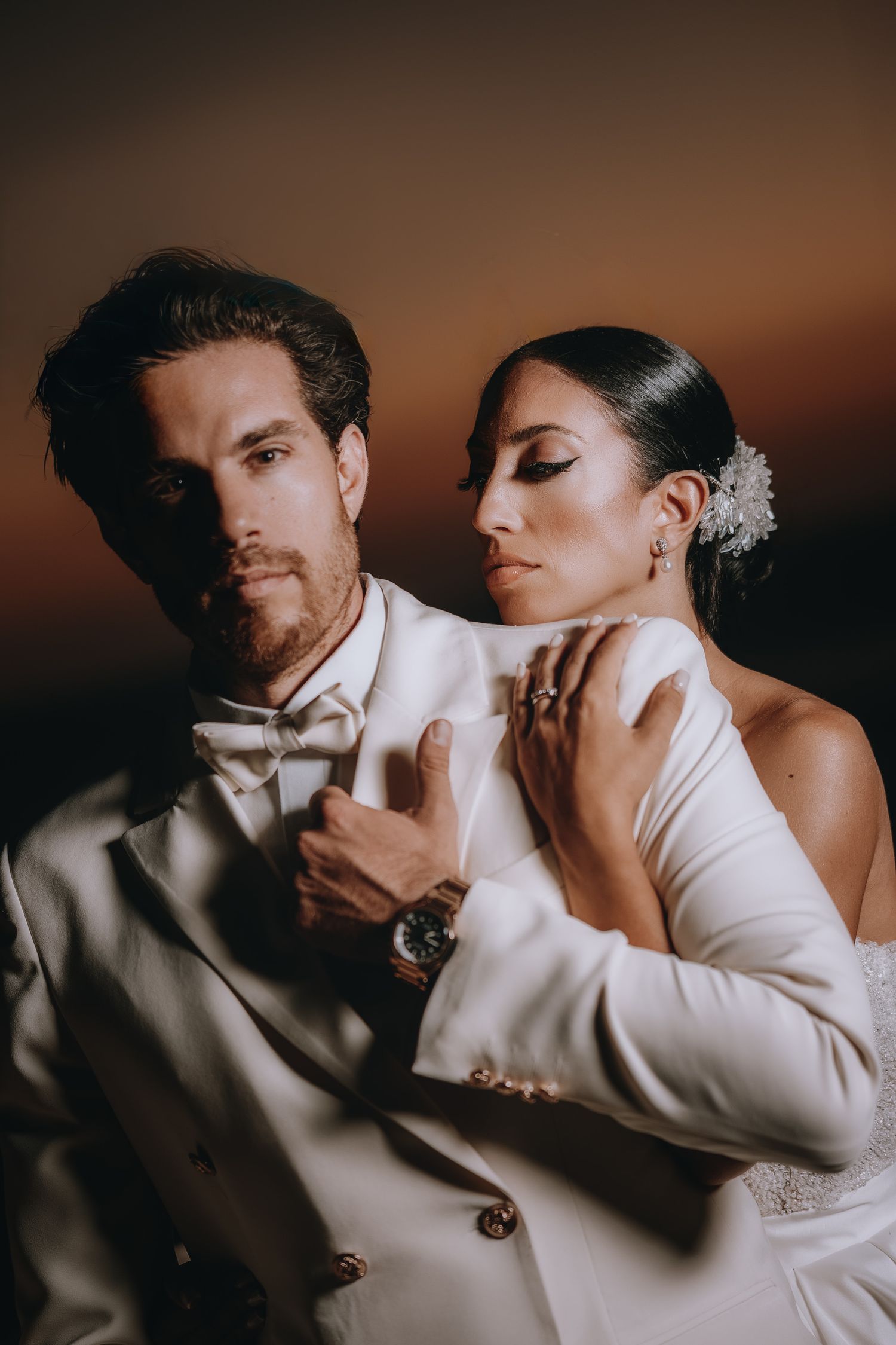 Intimate wedding portrait showing couple in white attire sharing tender moments against dark background.
