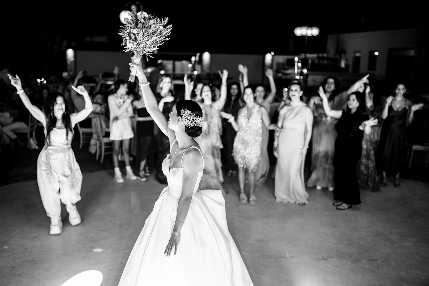 Wedding reception crowd cheering during bouquet toss in black and white photography.