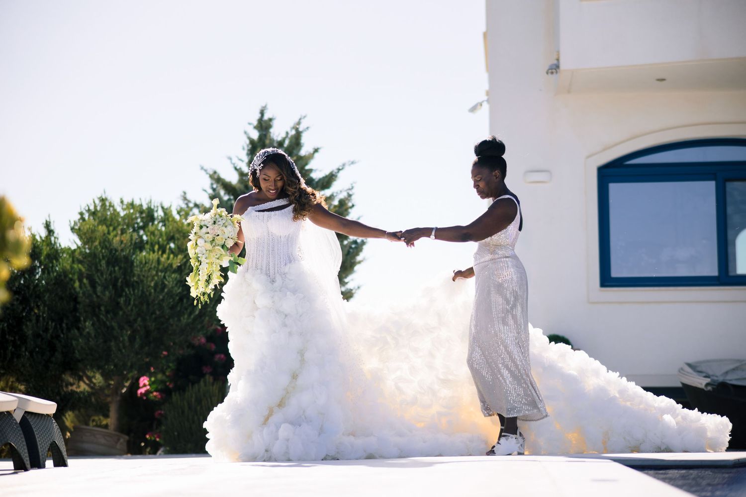 Wedding ceremony setup with white chairs and floral decorations against a bright outdoor backdrop.