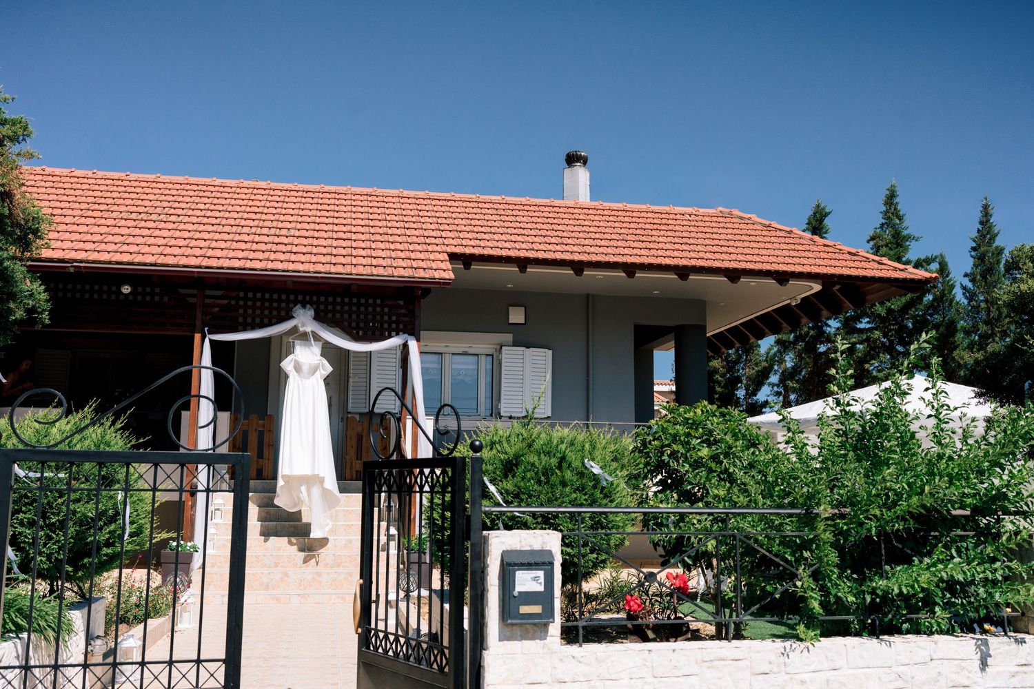 White wedding dress hanging outside Mediterranean style house with terracotta roof.