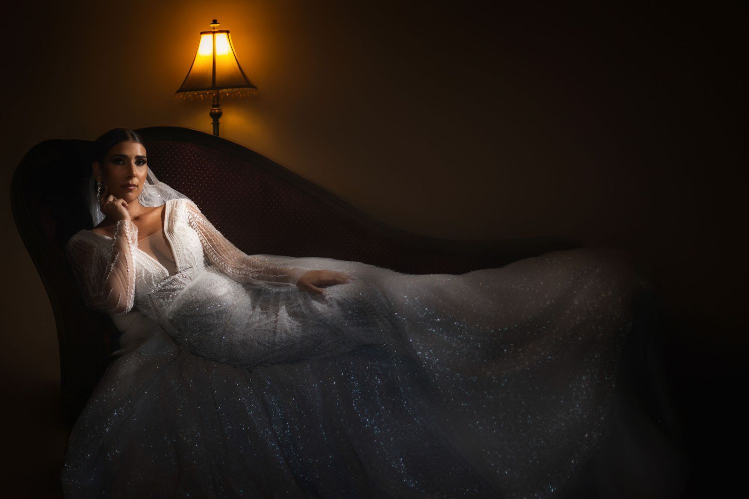 Dramatic bridal portrait with warm lamp lighting in a dark moody setting.