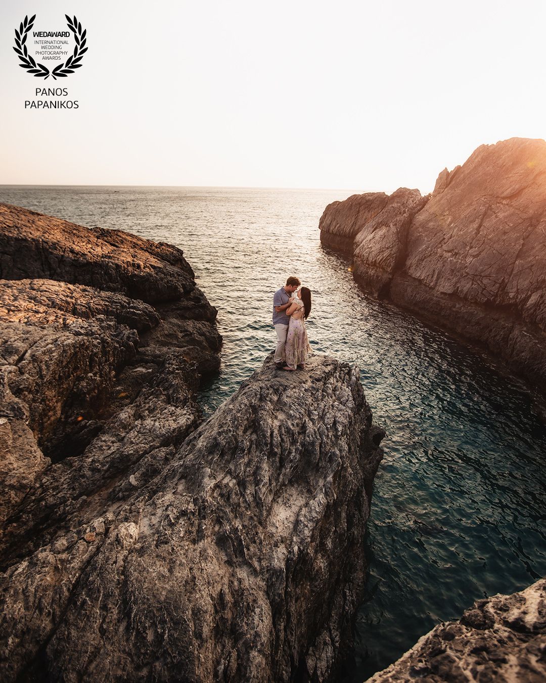 Wedding couple standing on dramatic coastal cliff overlook during golden hour.