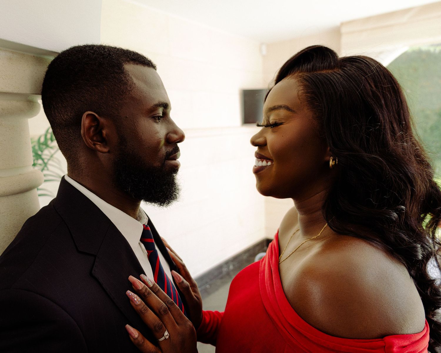 A couple in formal attire share a romantic moment, man in suit and woman in red dress gazing at each other.