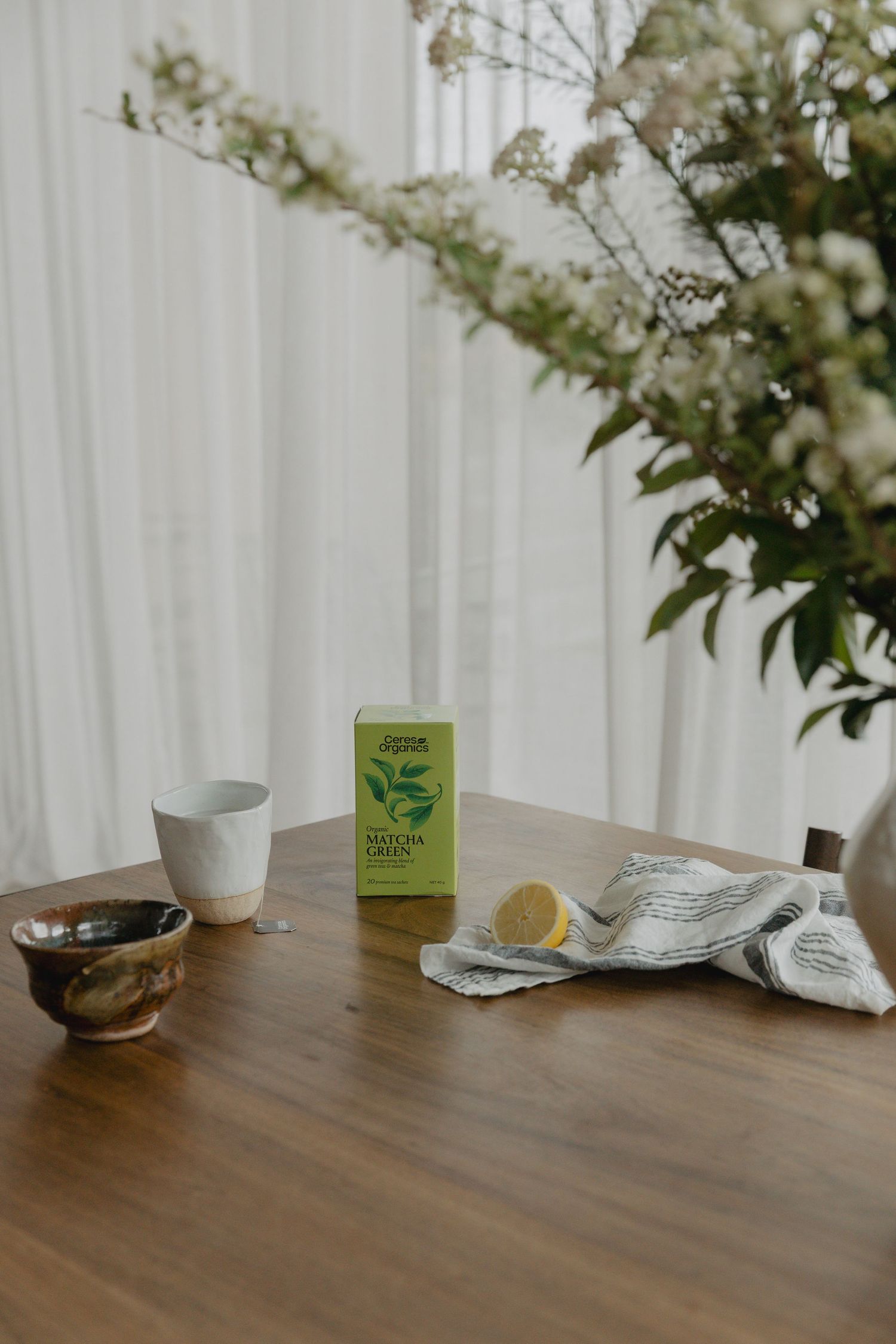 Minimalist table setting with tea boxes and white flowers in natural lighting.
