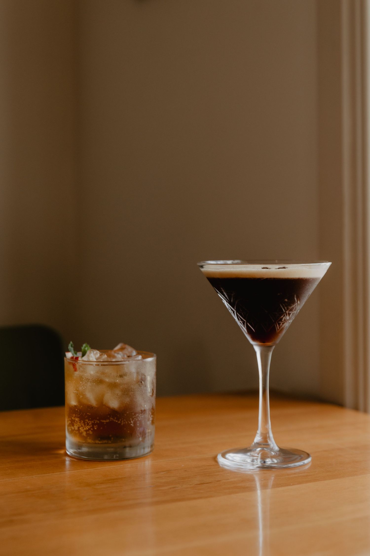 Three dark cocktails in elegant glassware on wooden table.