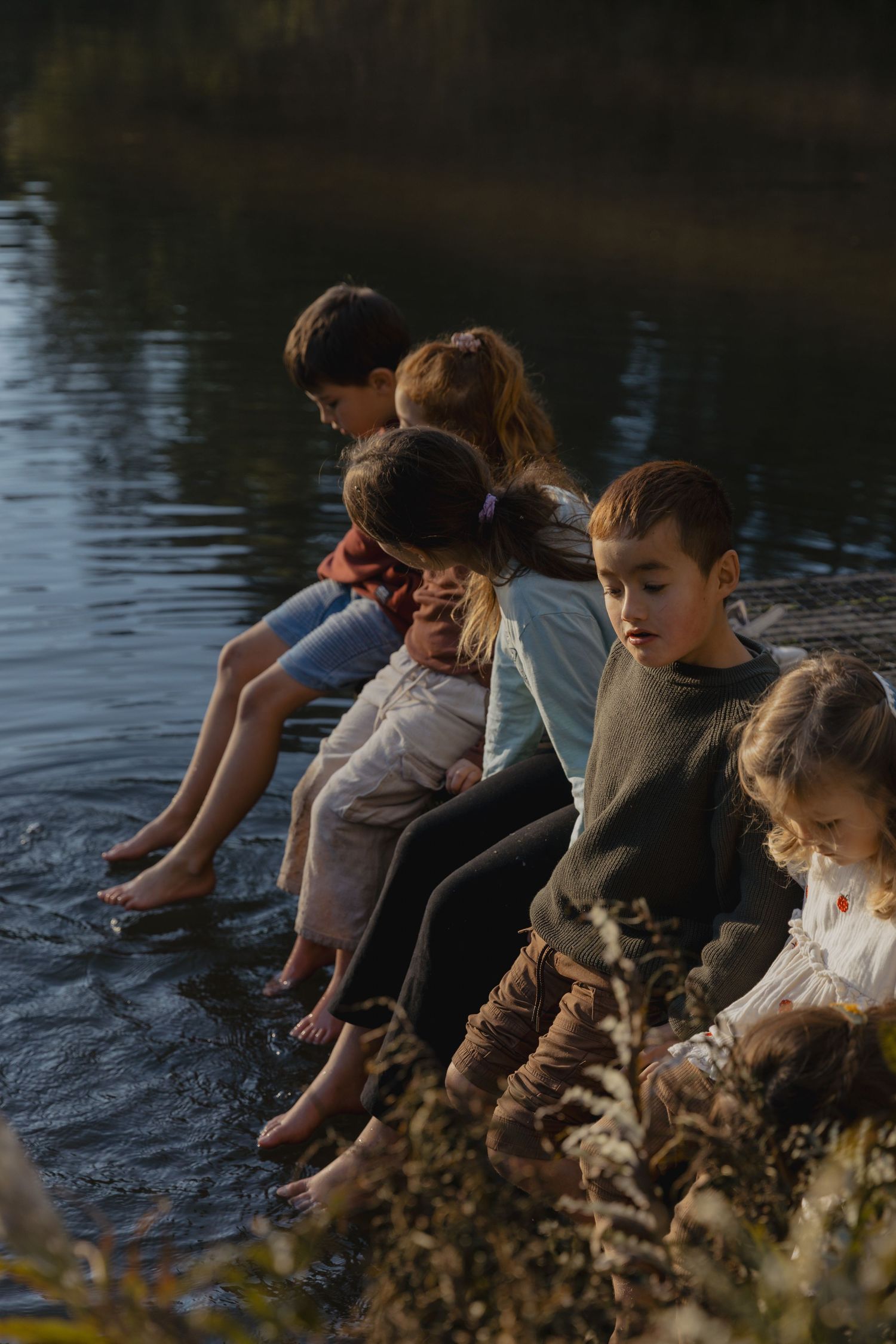 Group sitting by a lake at sunset with their feet dangling over the water.