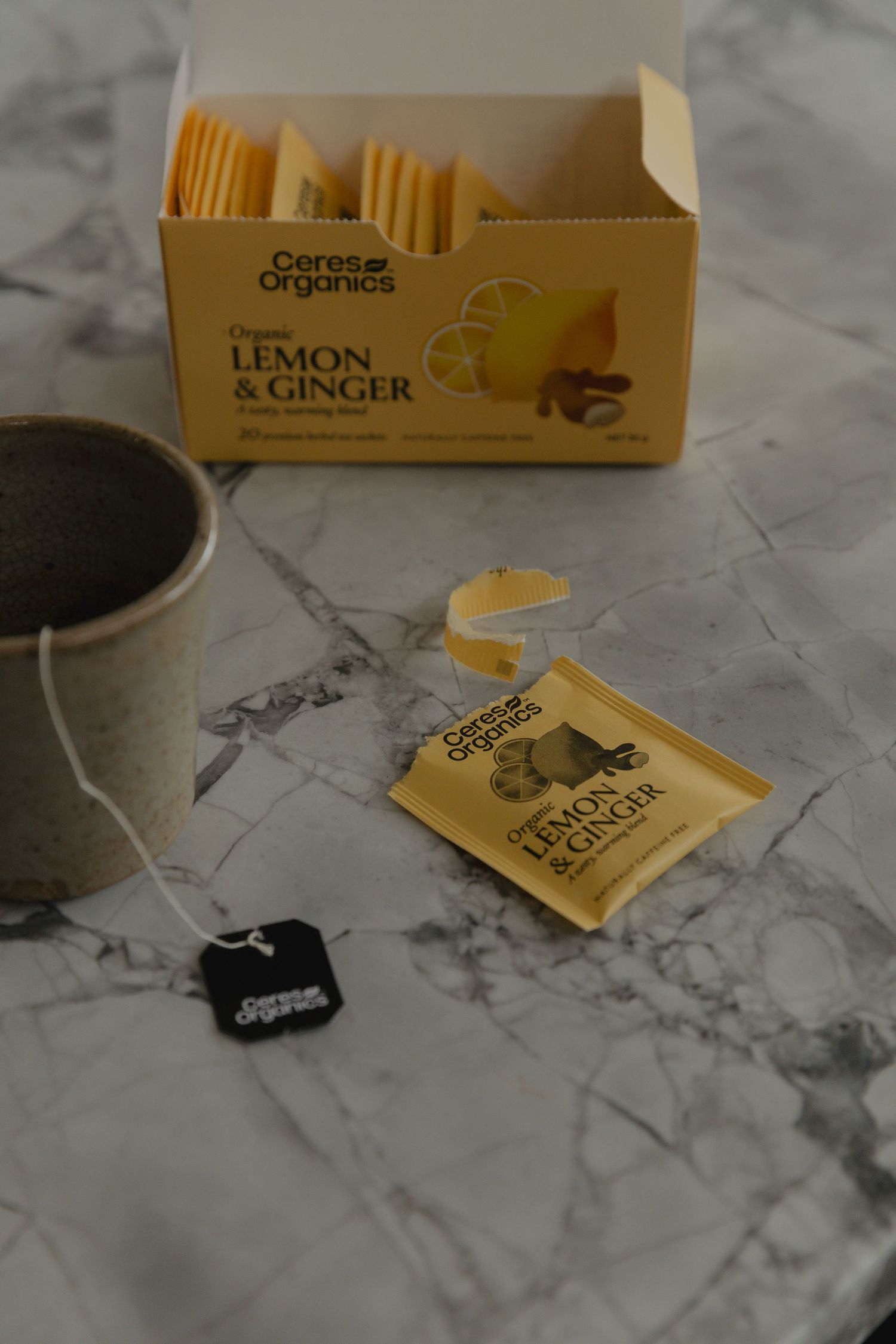 Lemon and ginger tea box and tea bags displayed on marble countertop.