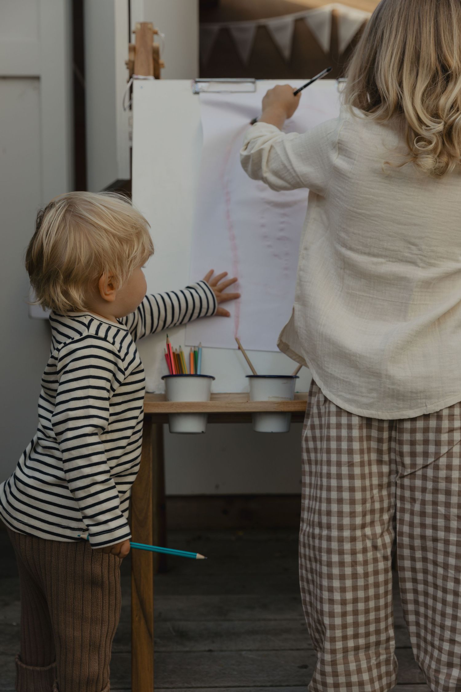 Two people drawing or writing on paper attached to a wall.
