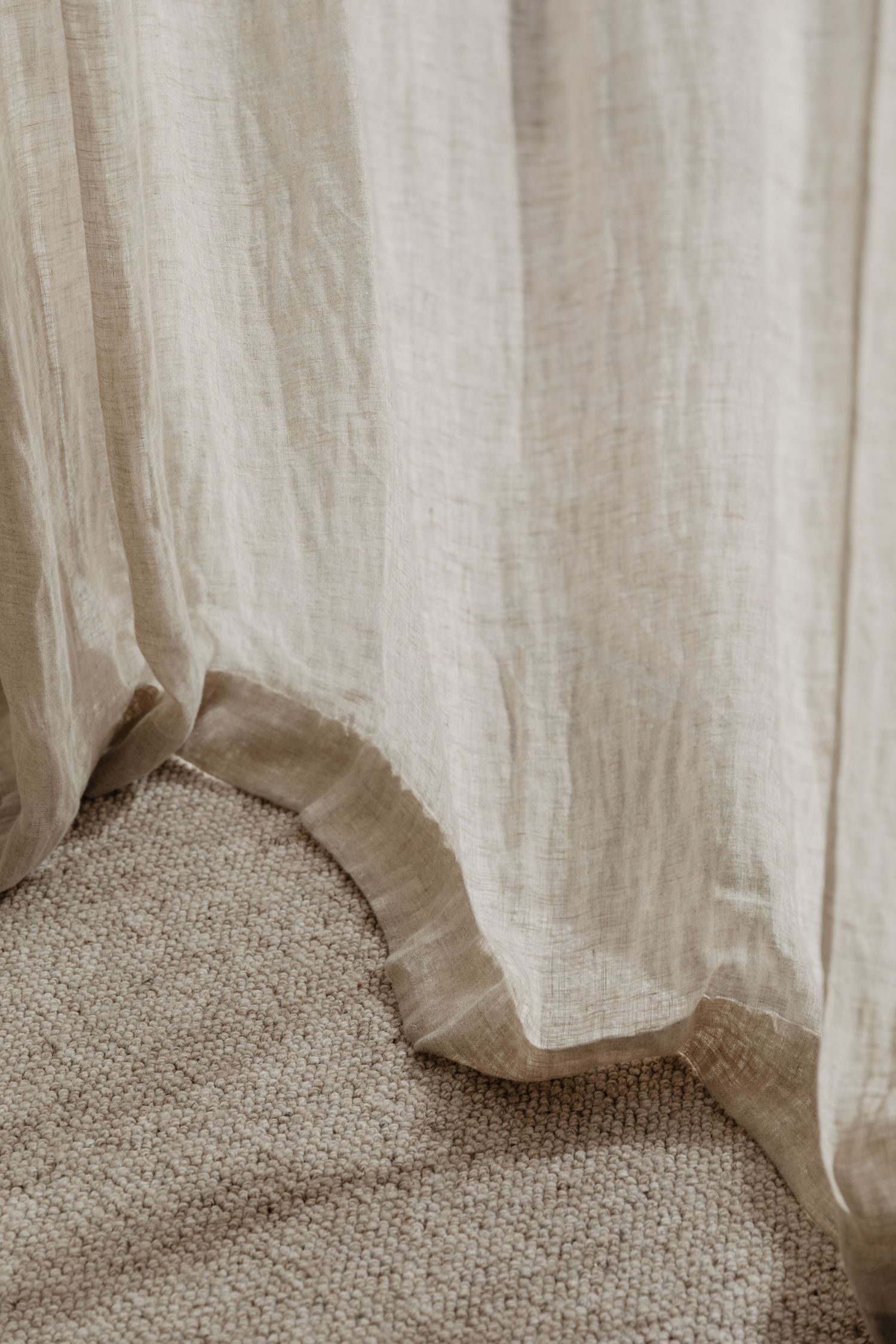 Close-up of linen curtain hem against textured carpet flooring.