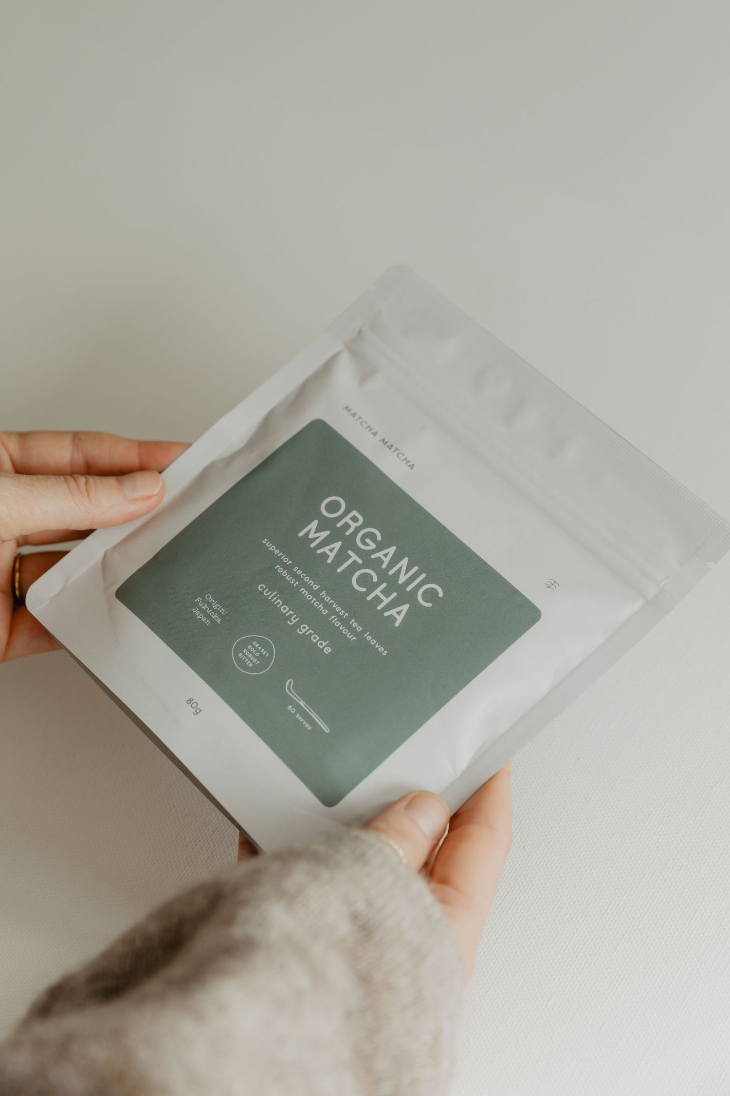 Hand holding white packaging pouch with organic matcha tea label.