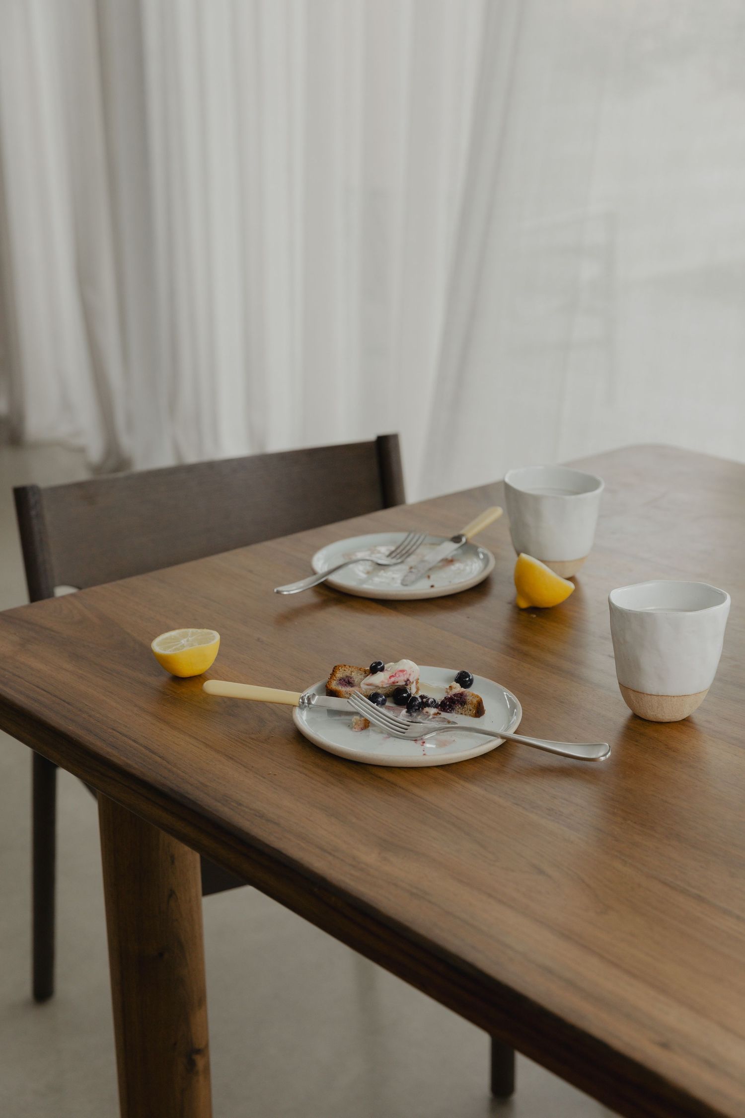 Minimalist wooden dining table with tea settings and citrus slice.