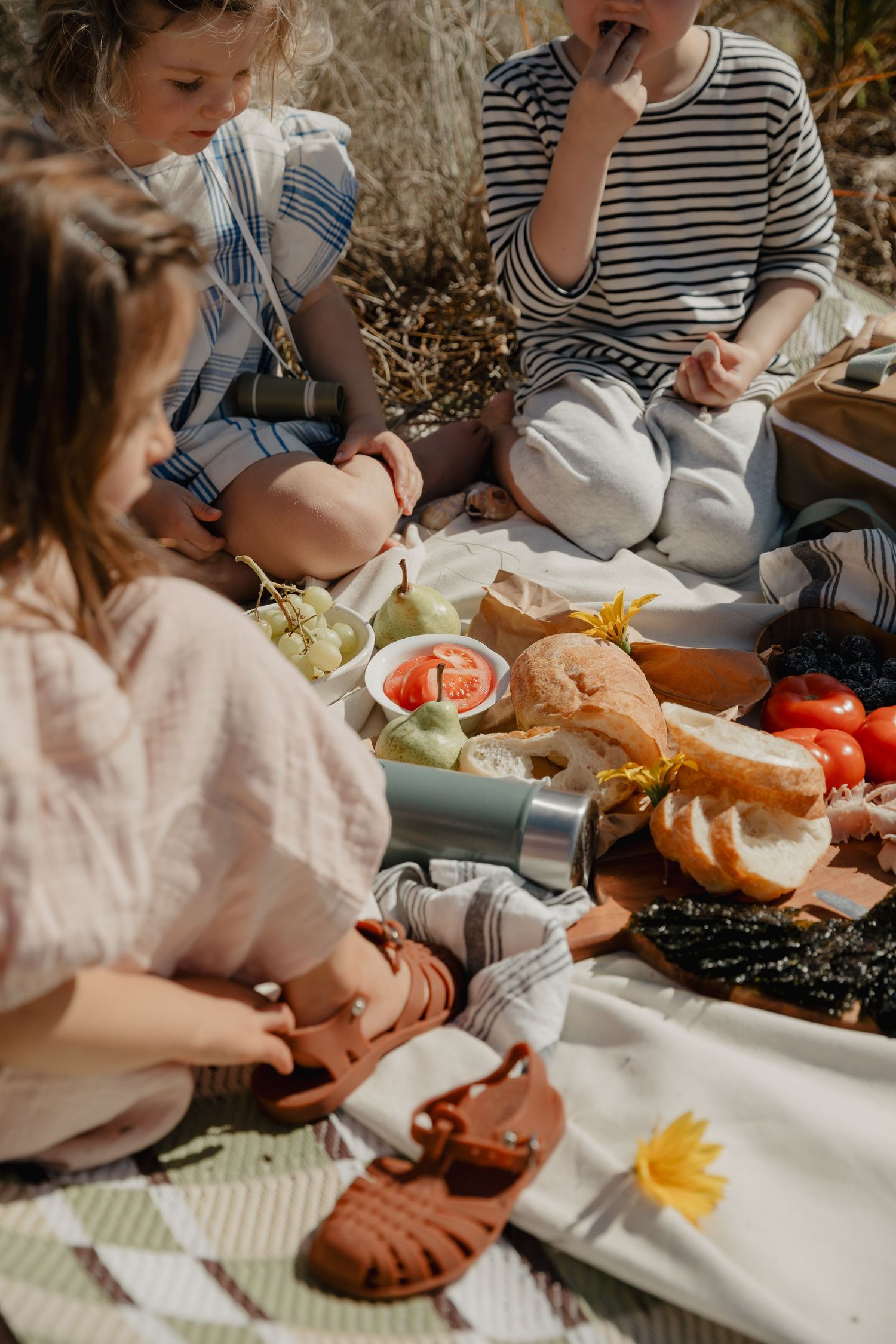 Children enjoying a picnic spread with sandwiches and fresh fruits on a white tablecloth.