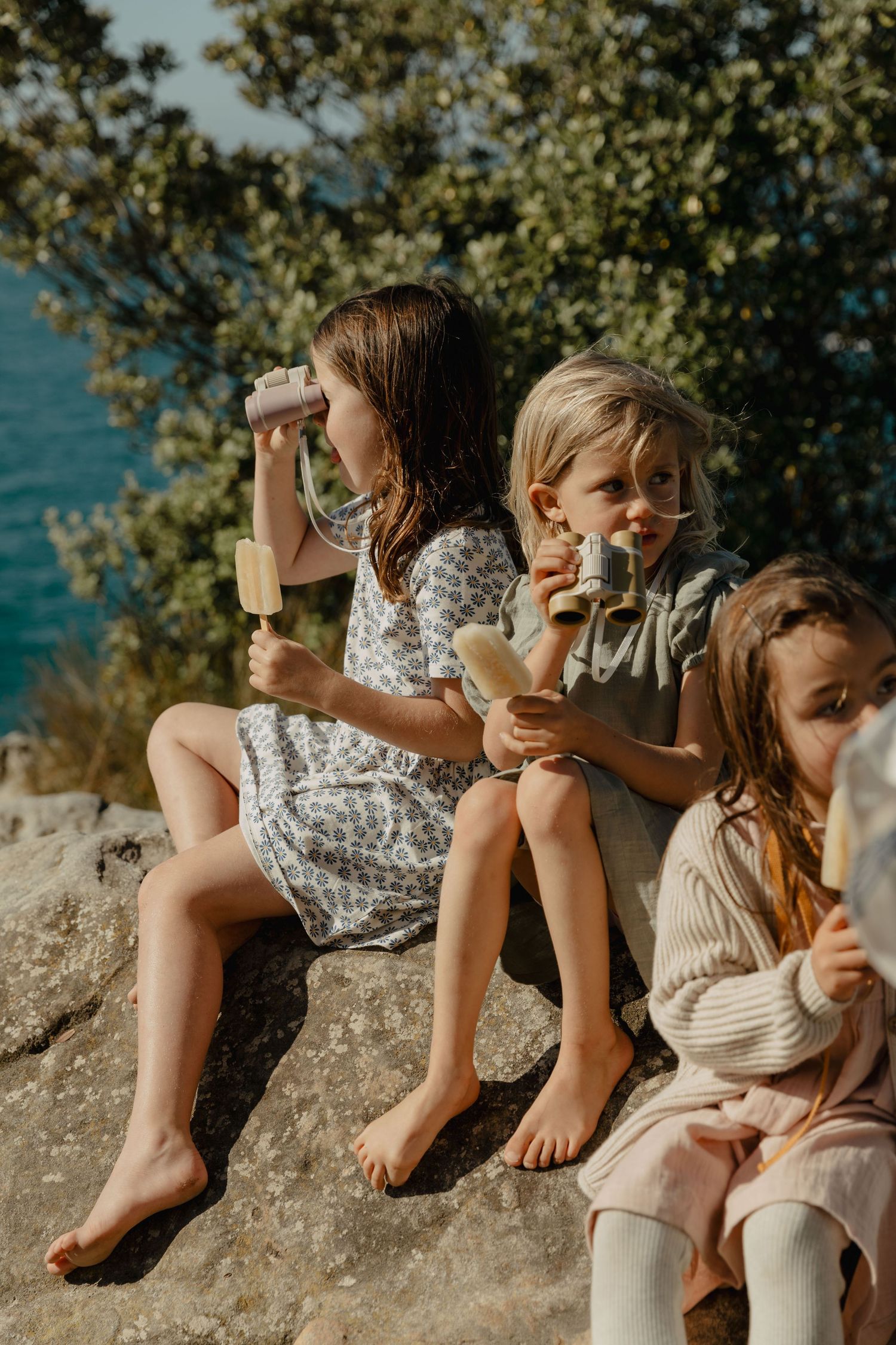 Children sitting together on coastal rocks near the ocean on a sunny day.