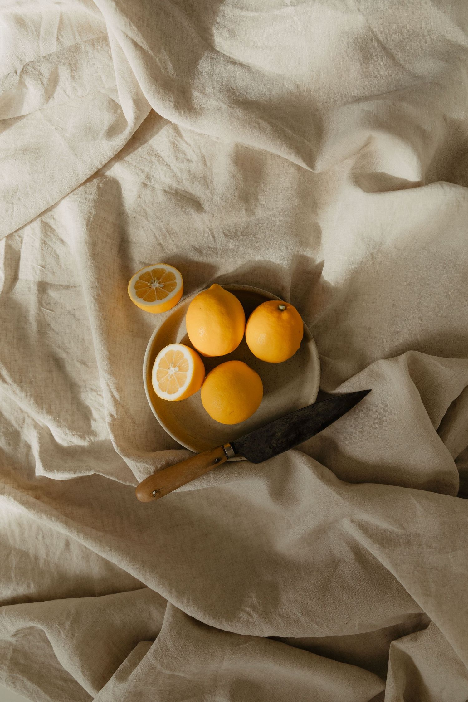 Fresh oranges and citrus fruits arranged on wrinkled beige linen fabric.