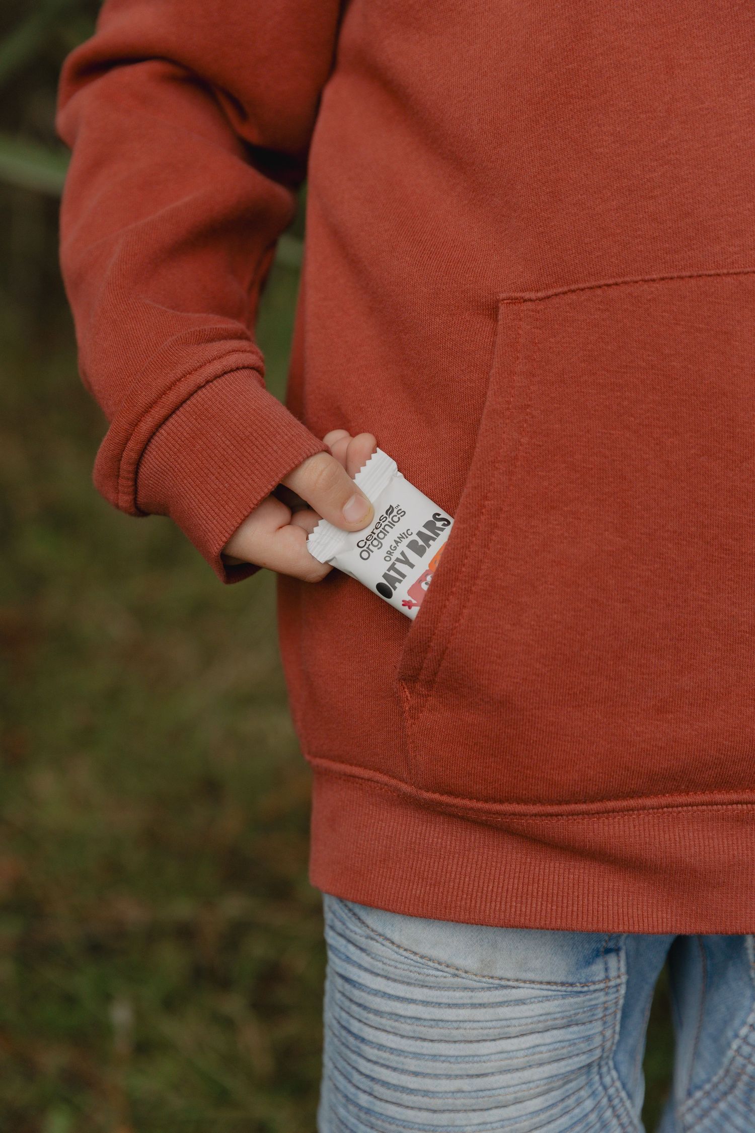 Close-up of rust-colored hoodie pocket and faded blue jeans and a muesli bar being pulled from the pocket.