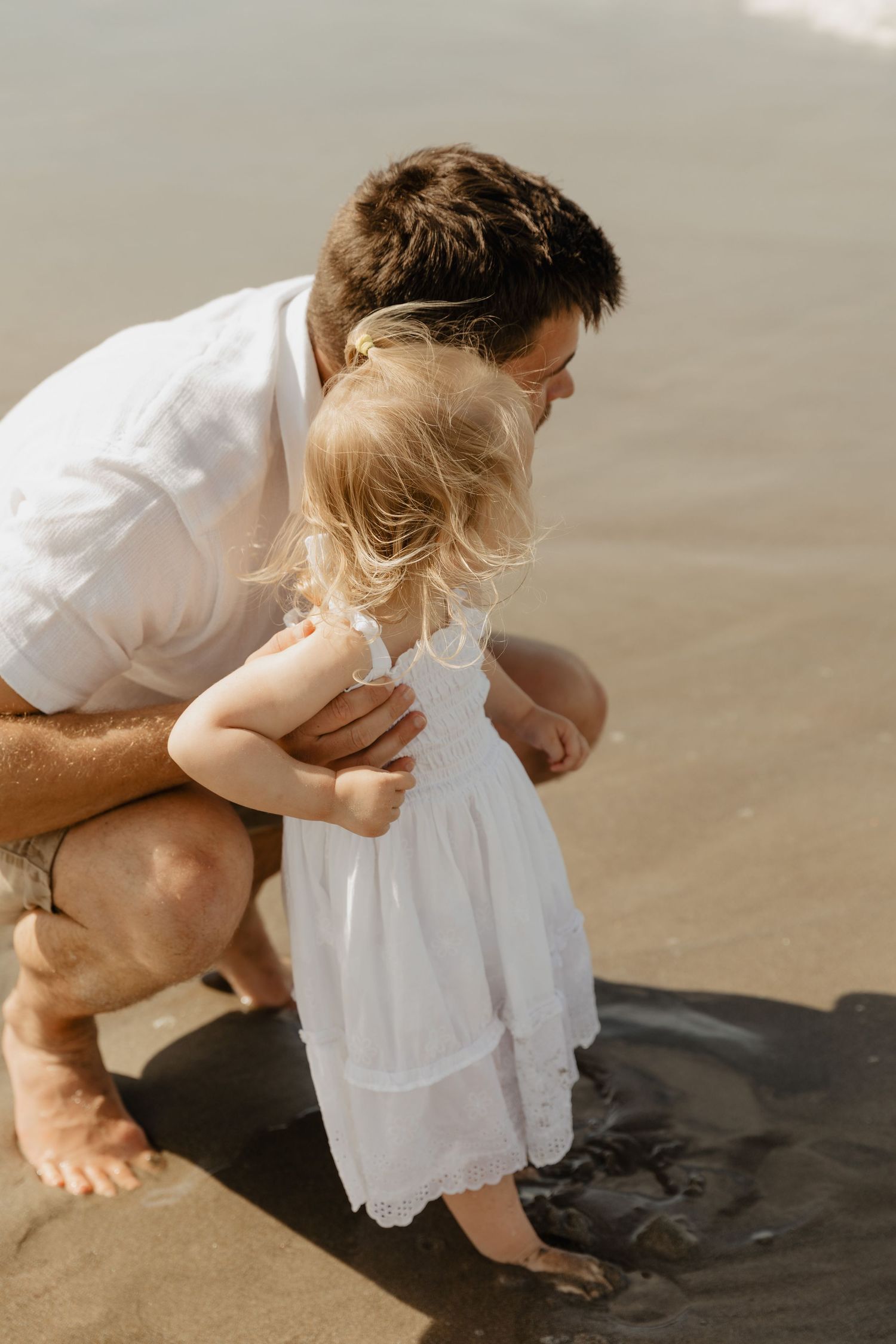 A tender moment between parent and child playing in the sand at the beach.