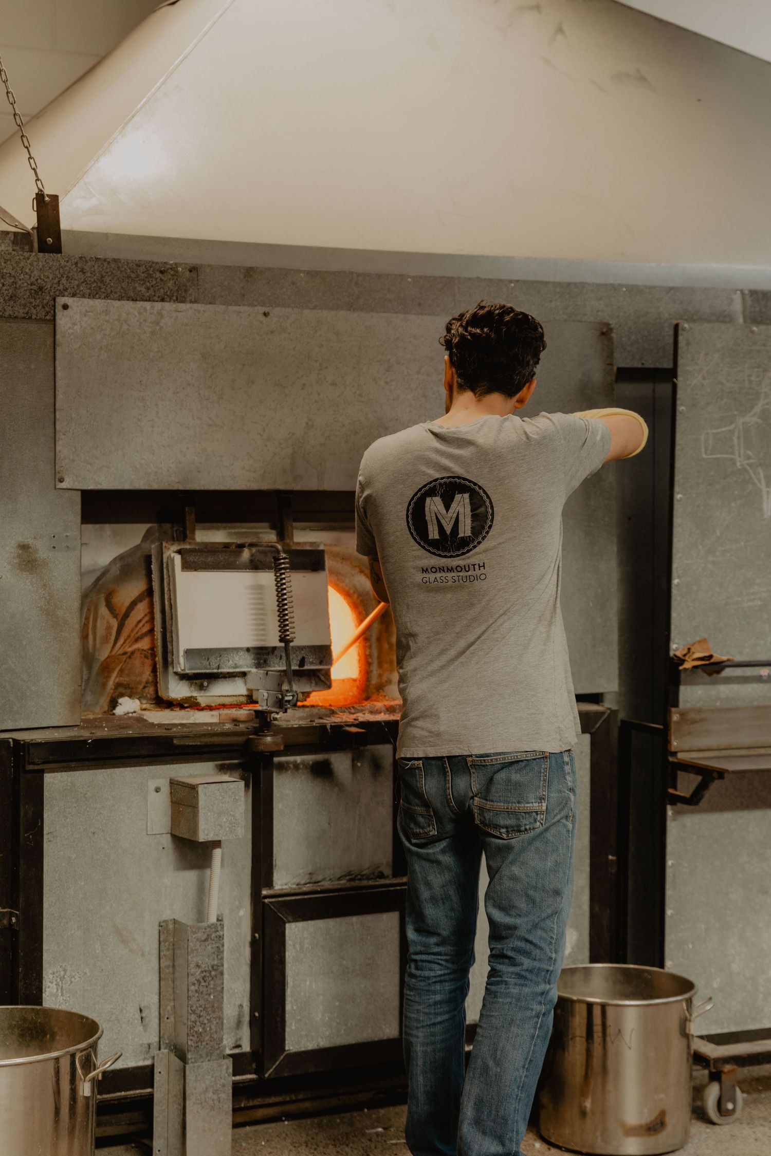 Worker in grey t-shirt with M logo cooking in industrial kitchen setting.