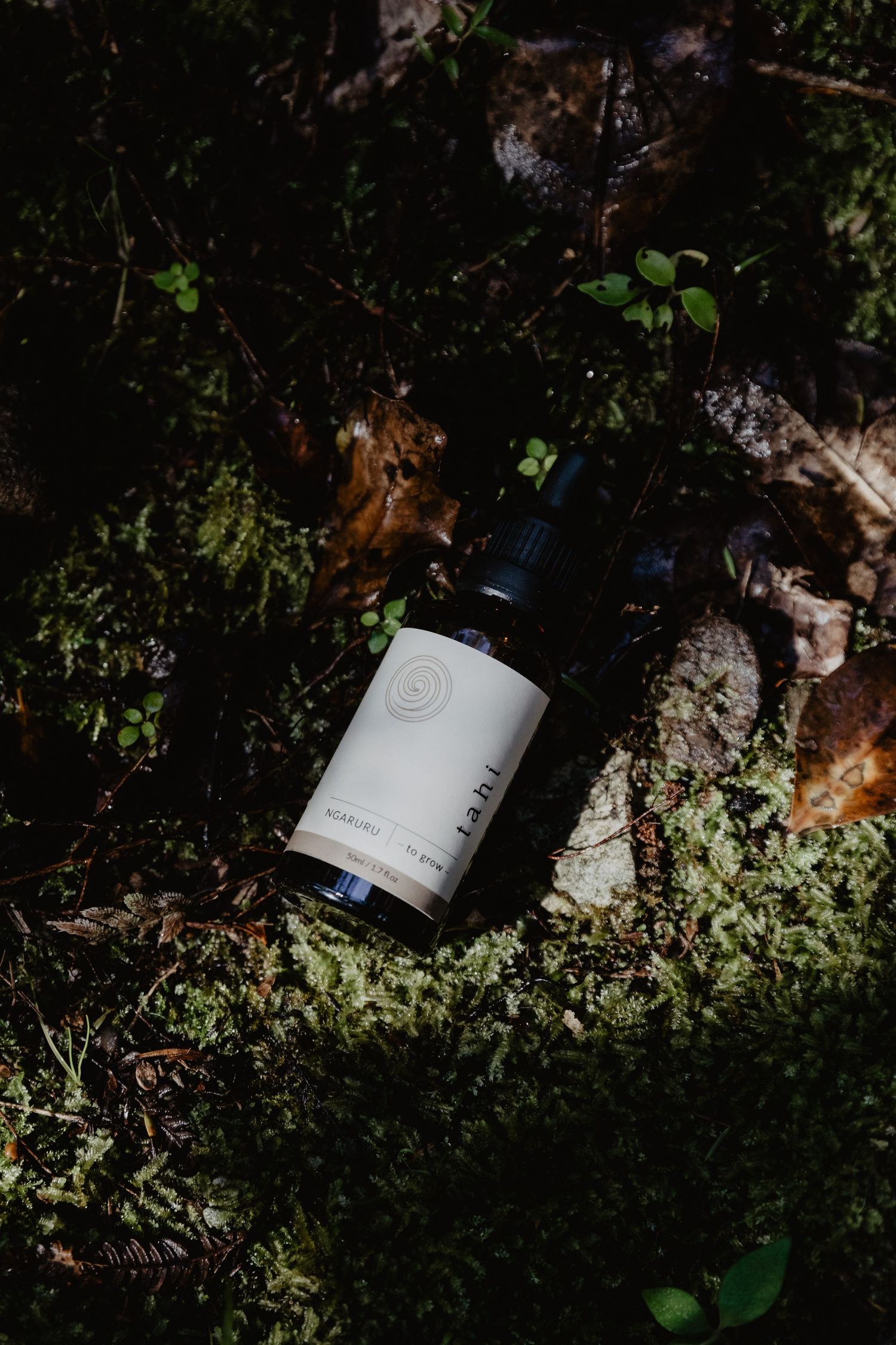 Small glass bottles of skincare with droppers arranged on natural mossy ground in dappled sunlight.