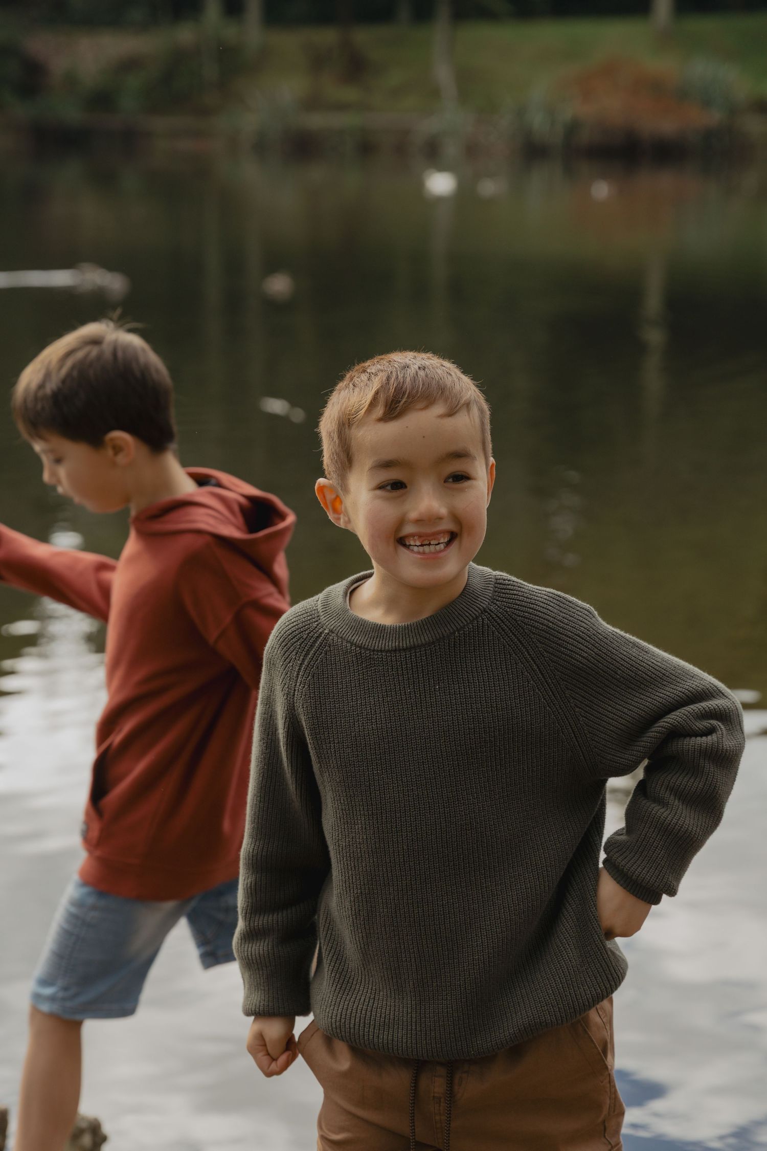 Children playing and laughing by a lake on an autumn day.