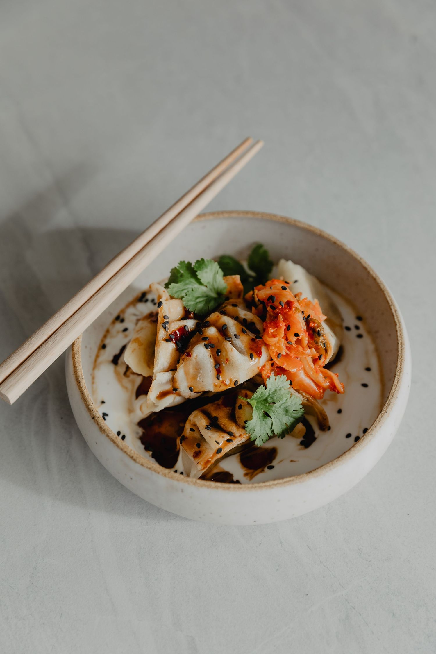 Asian dish with kimchi and garnishes served in a ceramic bowl with chopsticks.