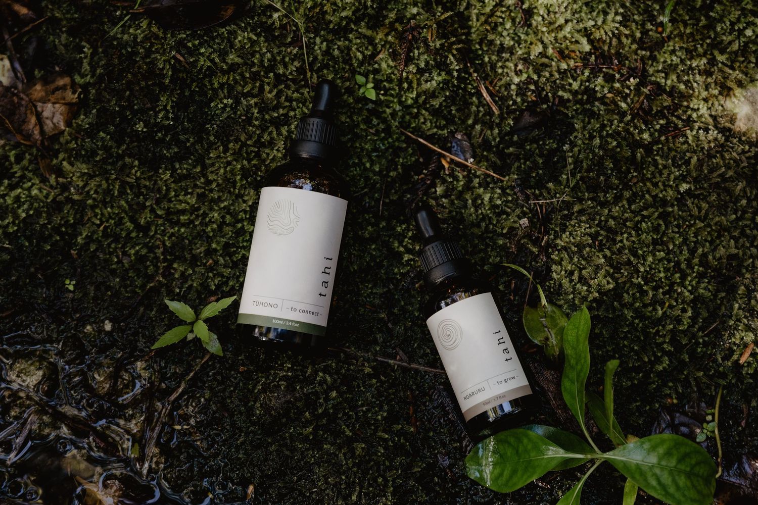 Two white product bottles lying on moss in natural outdoor lighting.