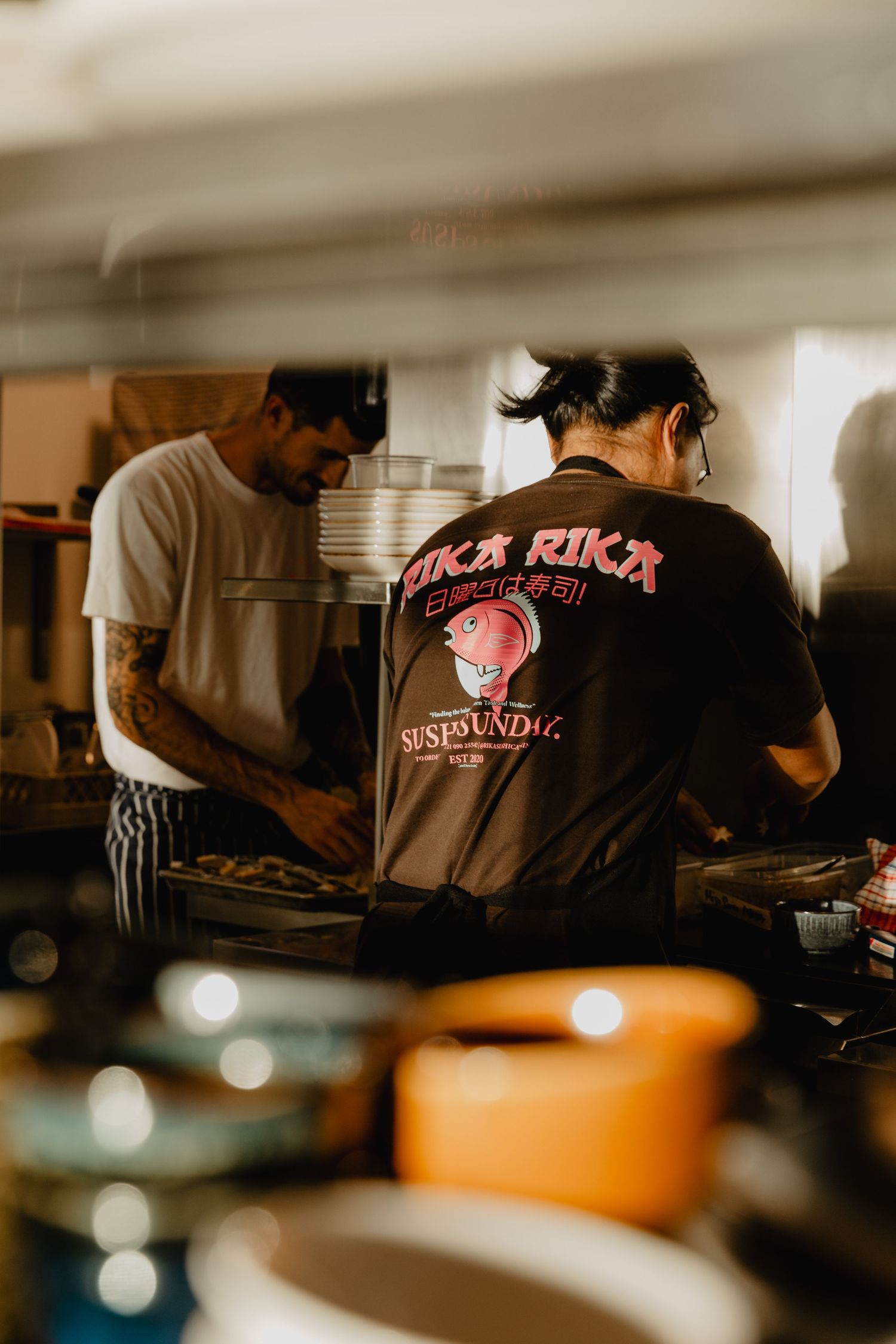 Chefs working in dimly lit restaurant kitchen wearing branded uniforms.