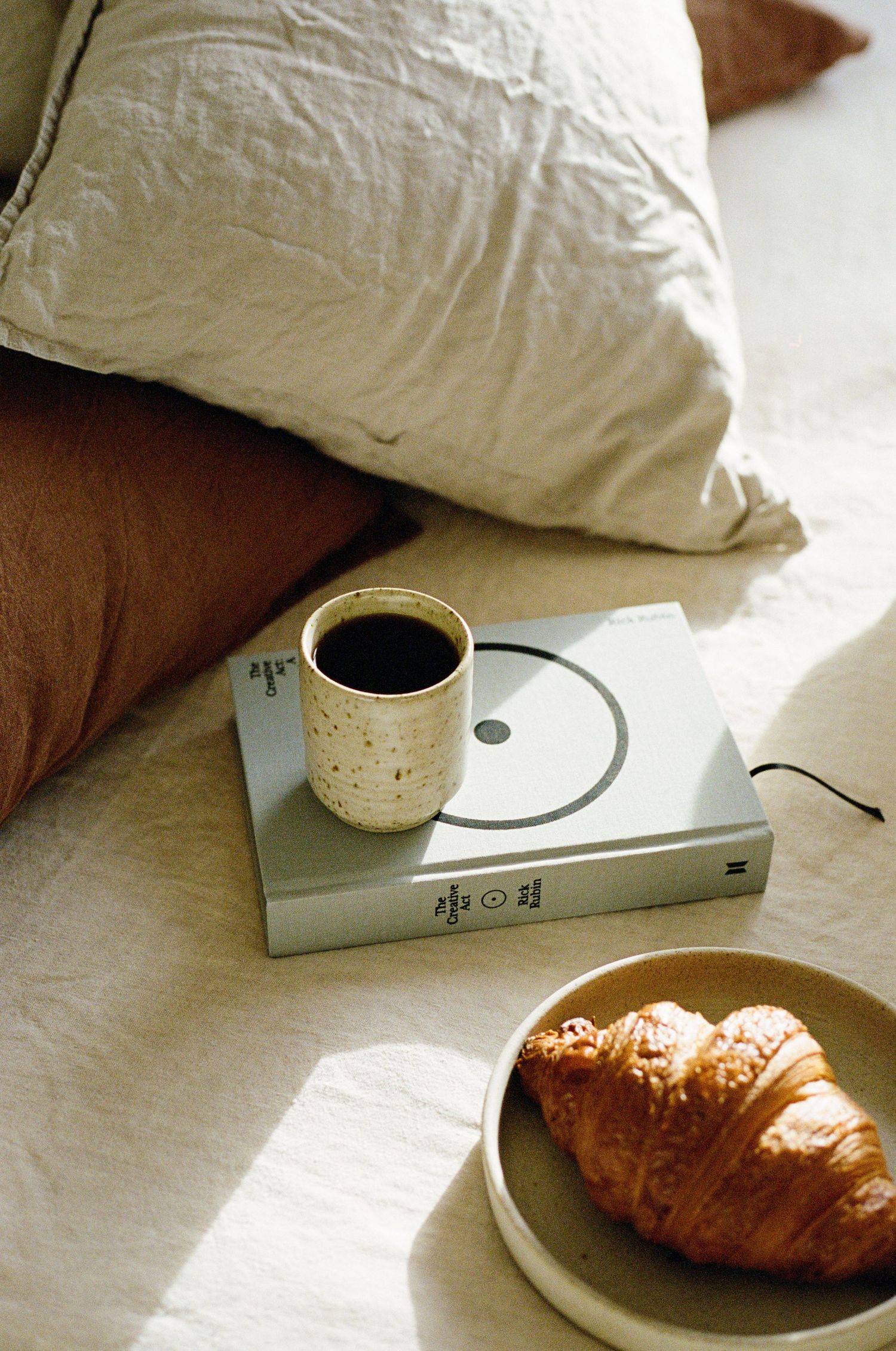 Coffee and croissant breakfast setup on white bedding with morning light.