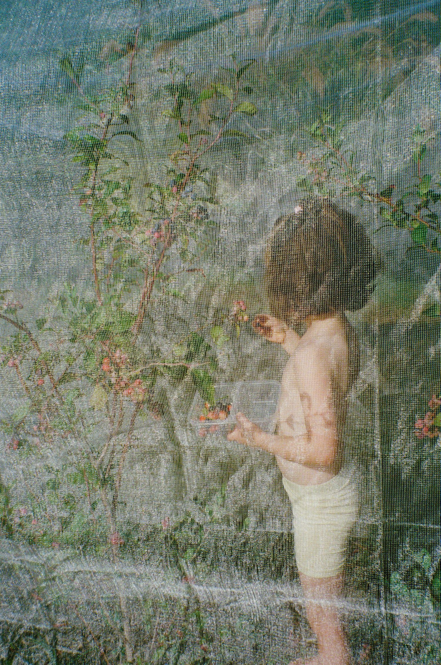 A dreamy vintage-style photograph showing a child in white picking berries against a textured wall.
