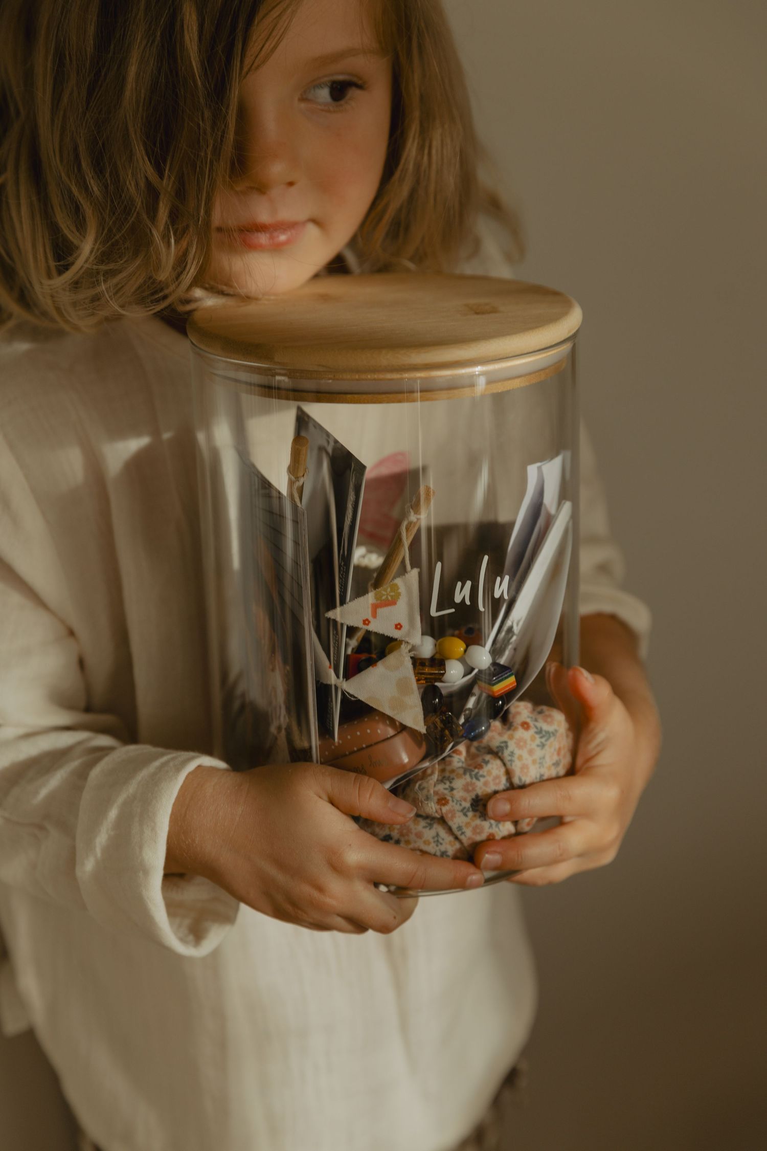 Hands holding a clear glass storage container with a wooden lid.